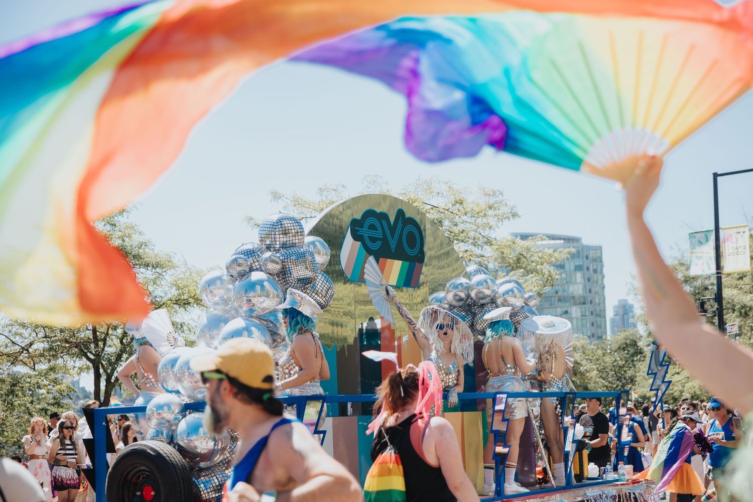 A colorful parachute canopy billows overhead as people gather beneath it during an outdoor community event.