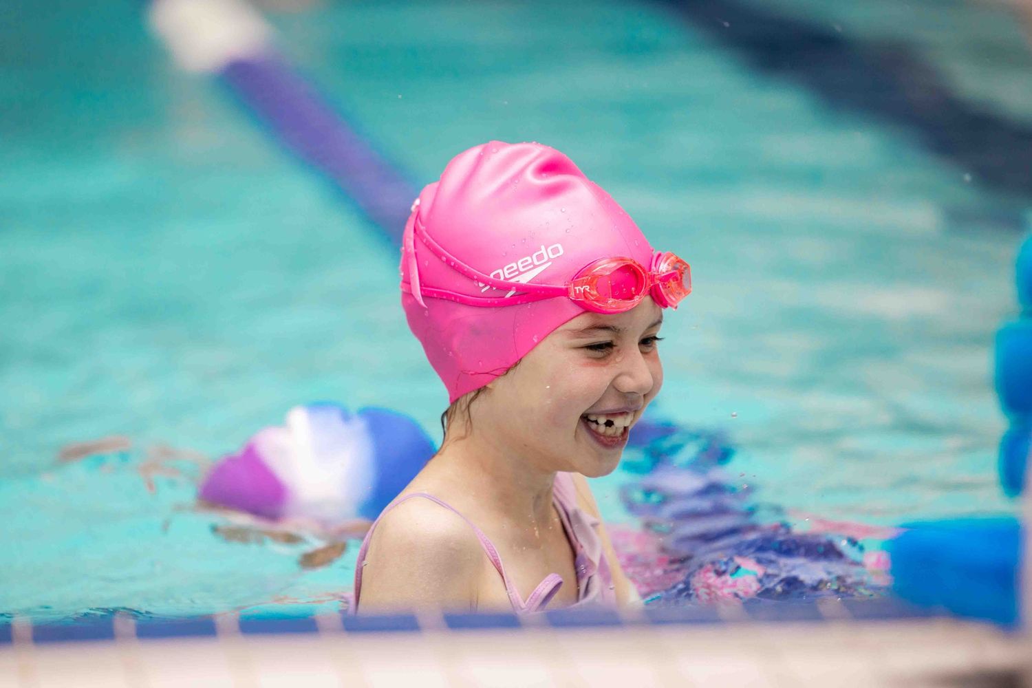 Young swimmer in a pink cap enjoying time in a bright blue pool.