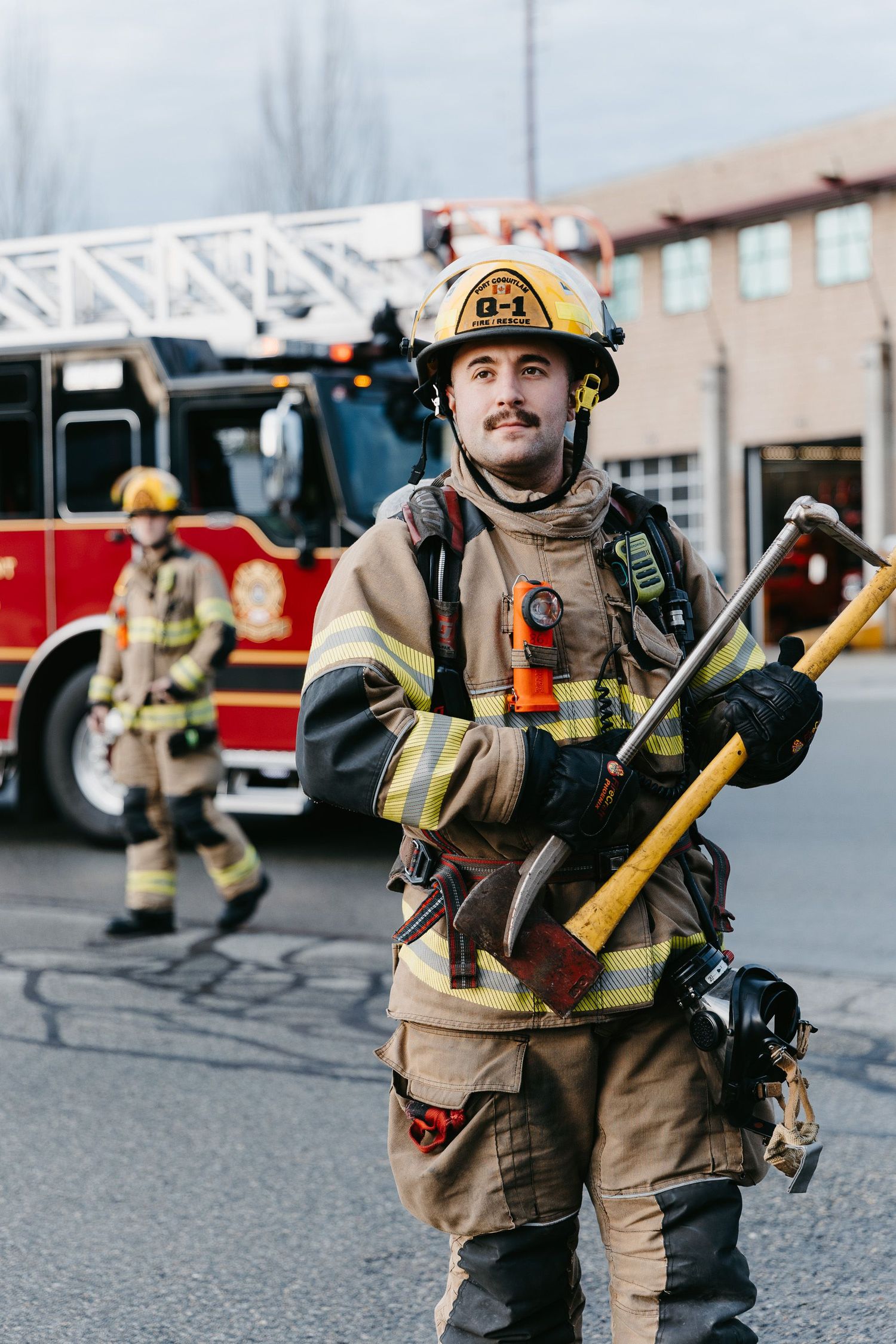 Firefighters in full gear carrying equipment across a parking lot.