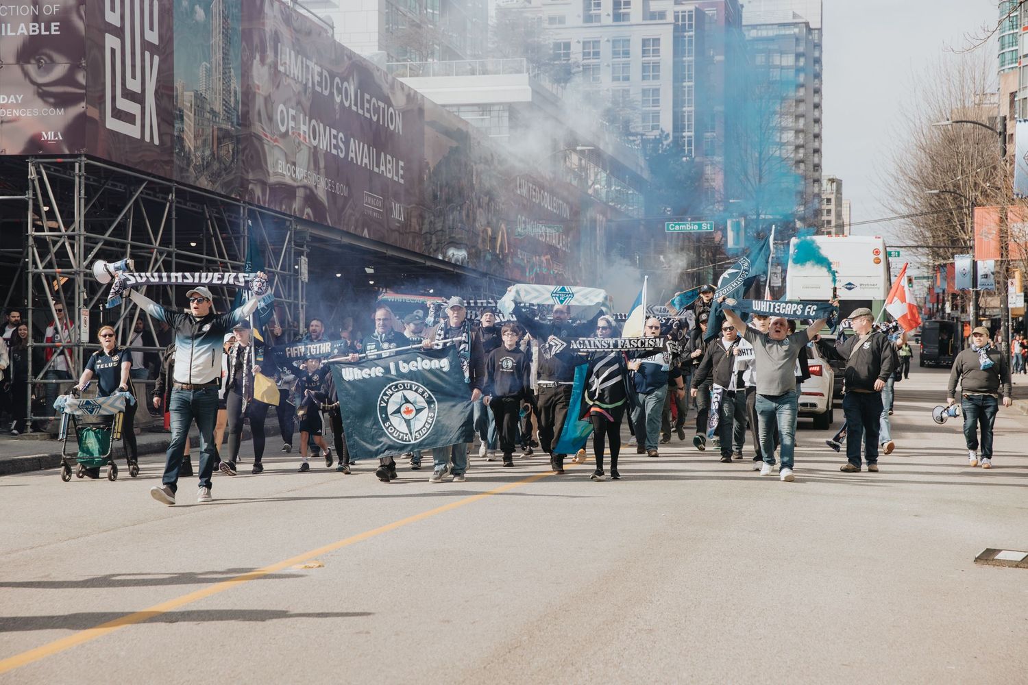Soccer supporters march through city streets carrying flags and creating smoke effects.