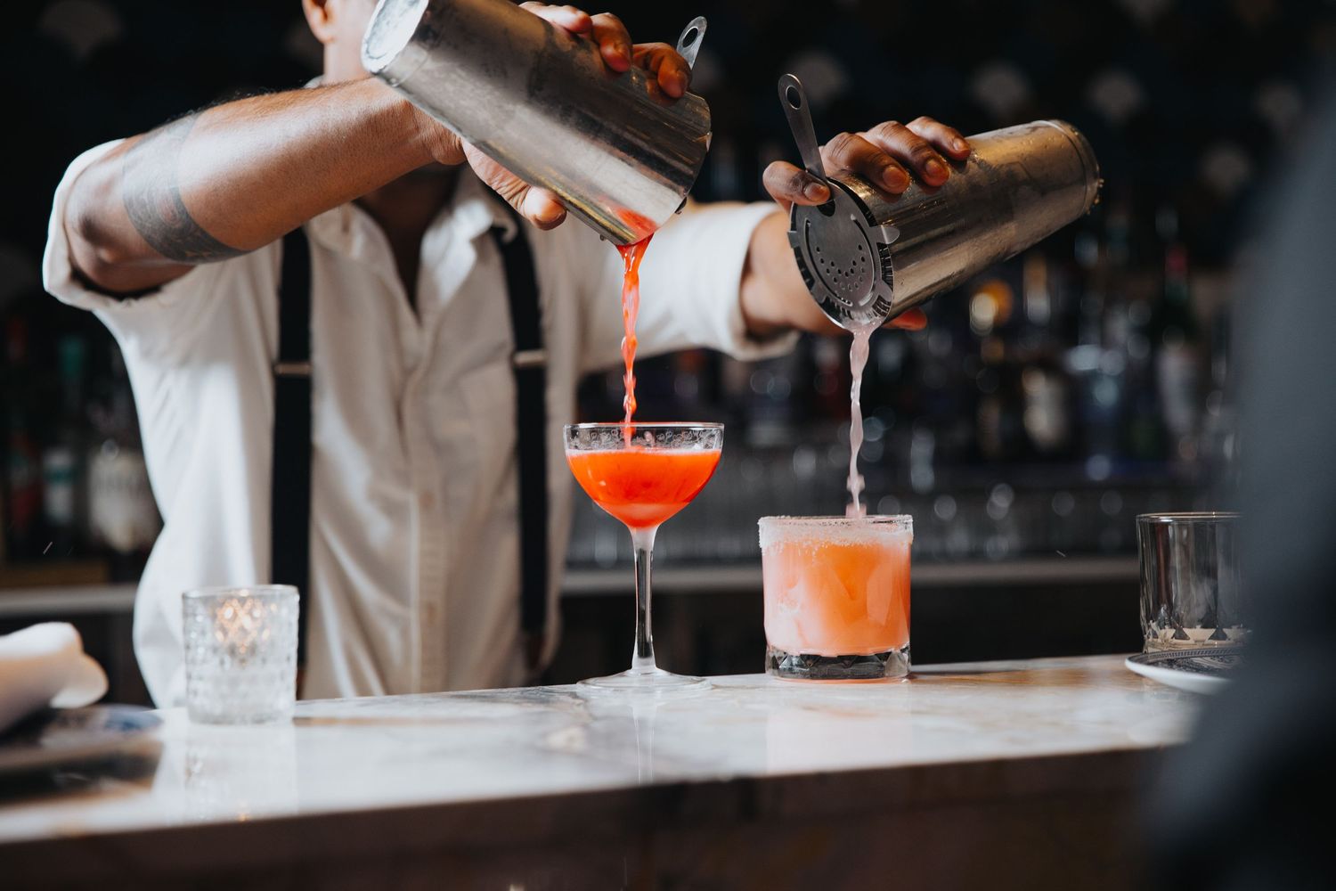 Bartender pouring colorful cocktails at upscale bar counter.