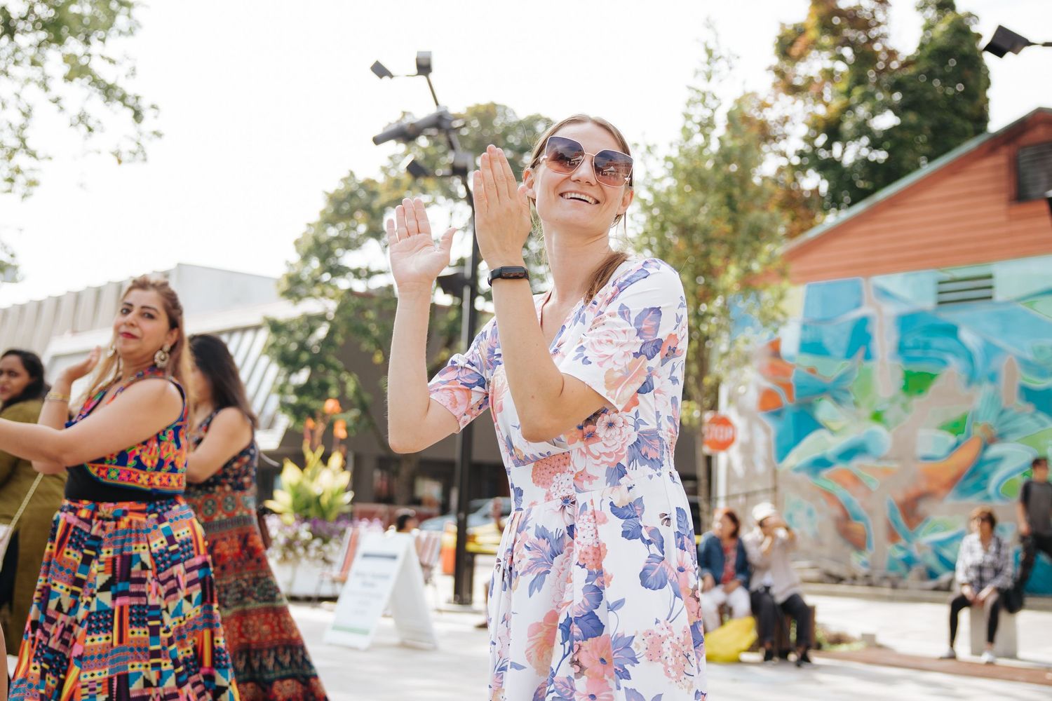 People dancing at an outdoor festival with colorful mural in background.