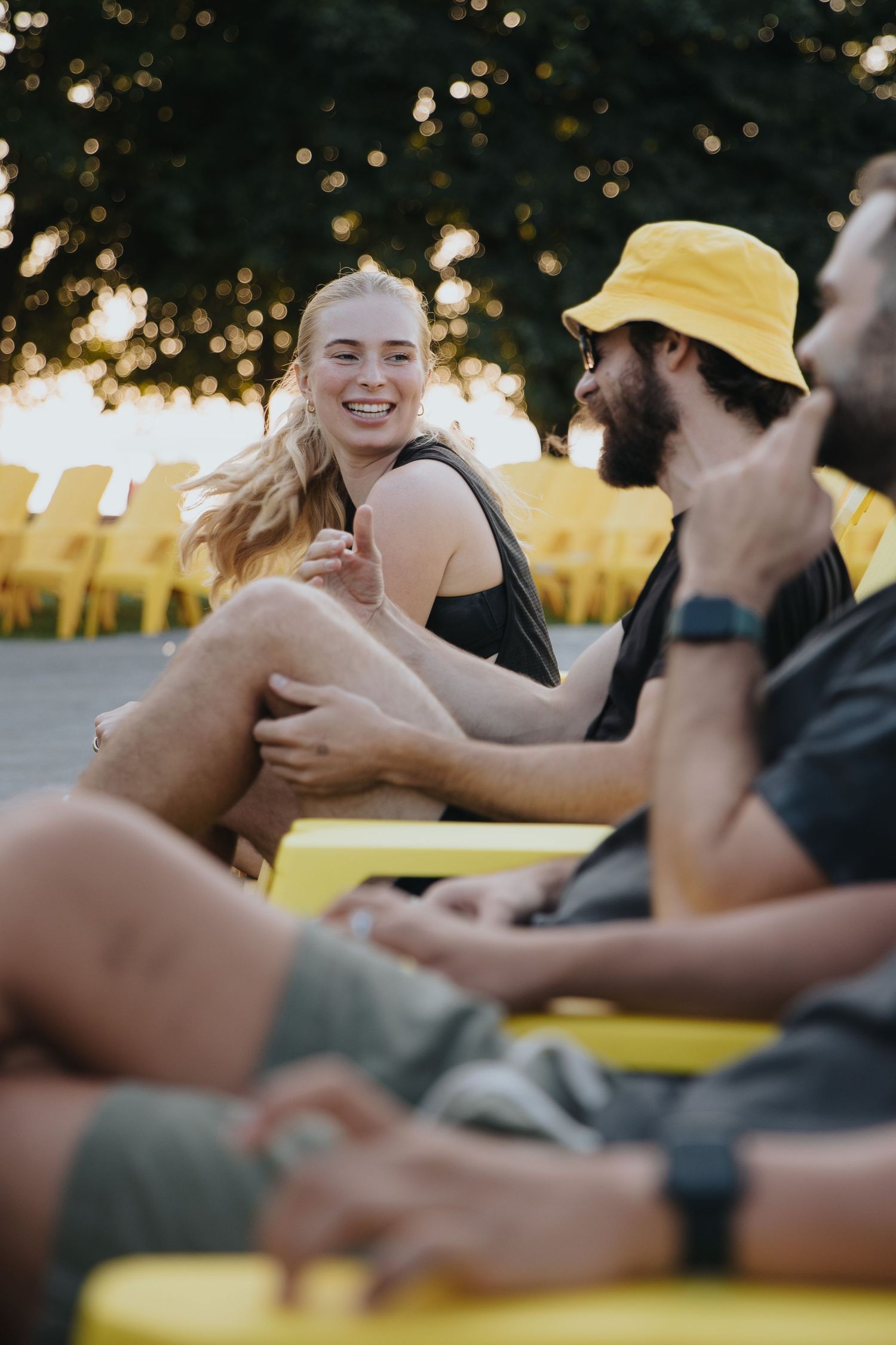 Group of young friends laughing and relaxing on yellow chairs outdoors at sunset.
