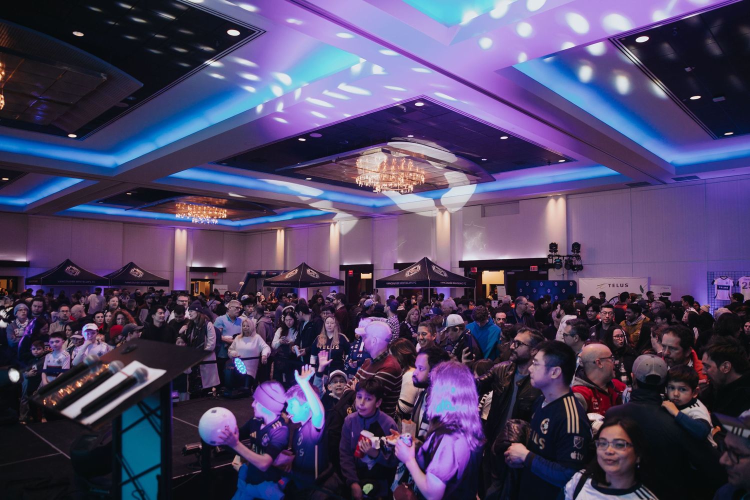 Large conference hall illuminated with purple and blue lighting while filled with attendees.