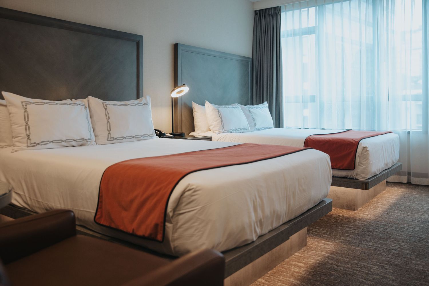 Elegant hotel room with two queen beds featuring white pillows and orange accent blankets.