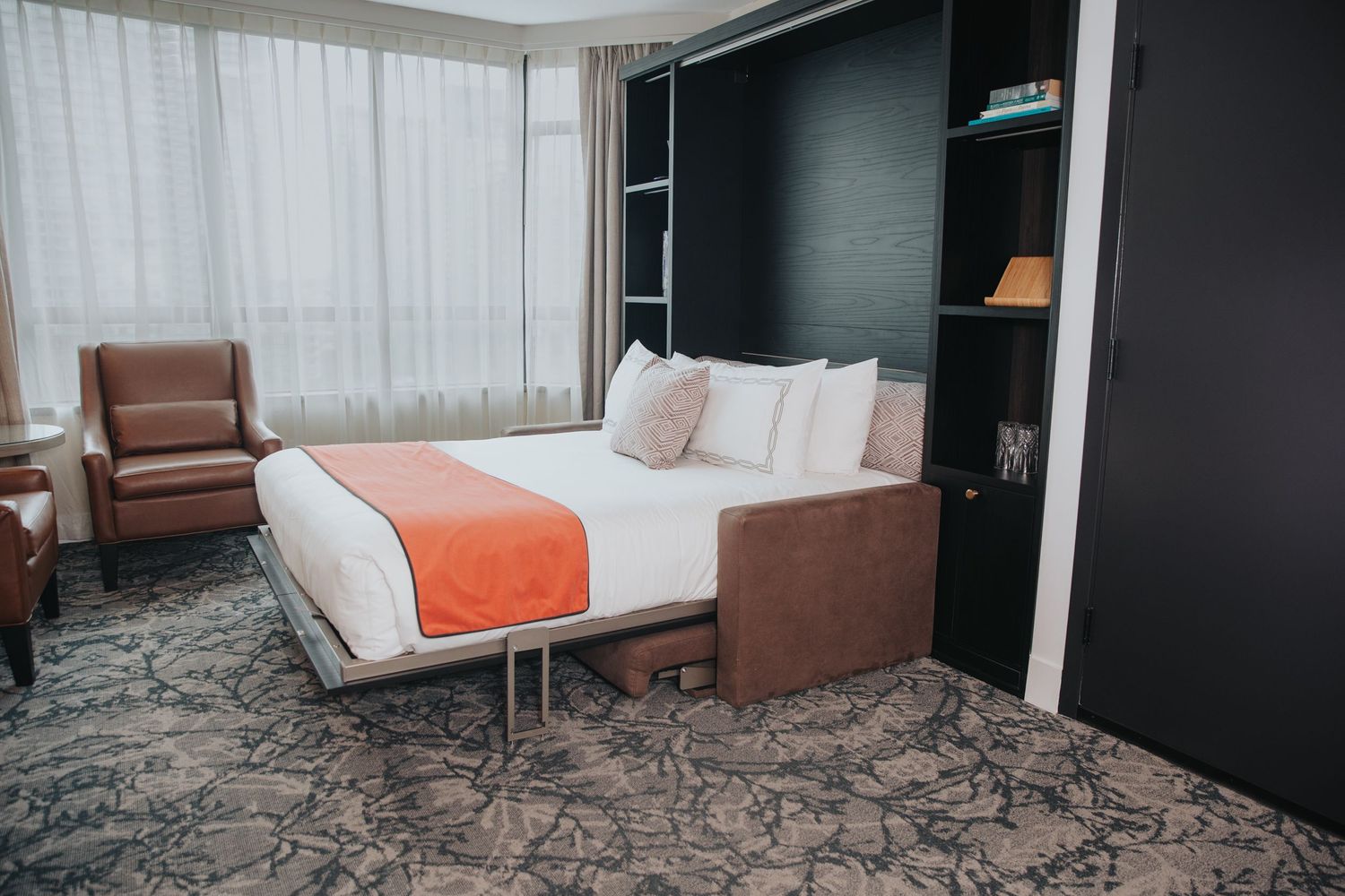 Contemporary hotel room with orange accent pillows and minimalist decor.
