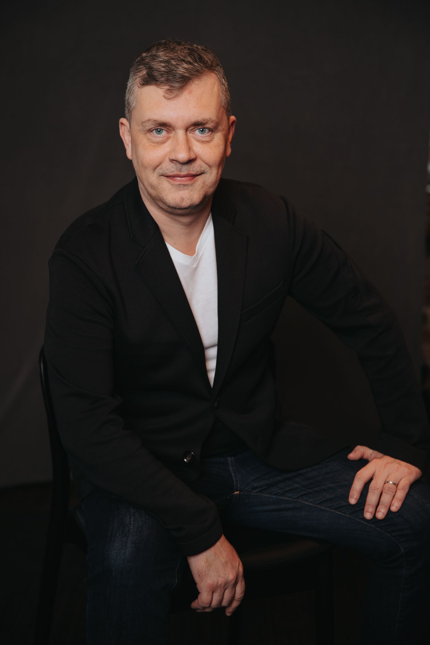 Studio portraits in black jacket and white shirt against dark backdrop.