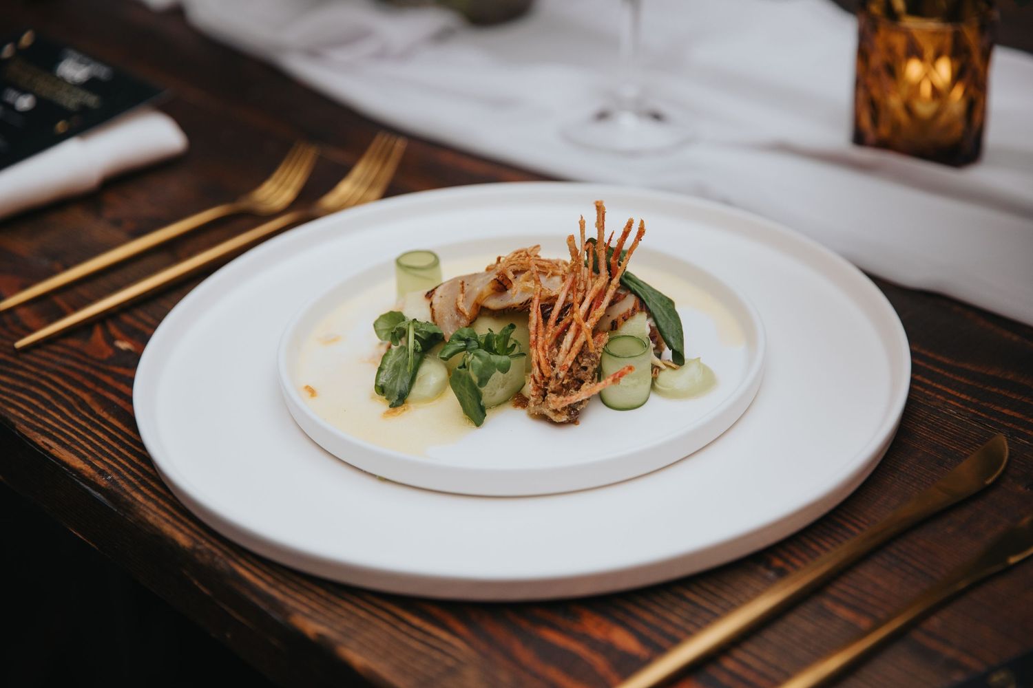 Elegant white plates with gourmet food presentations on a dark wooden table.