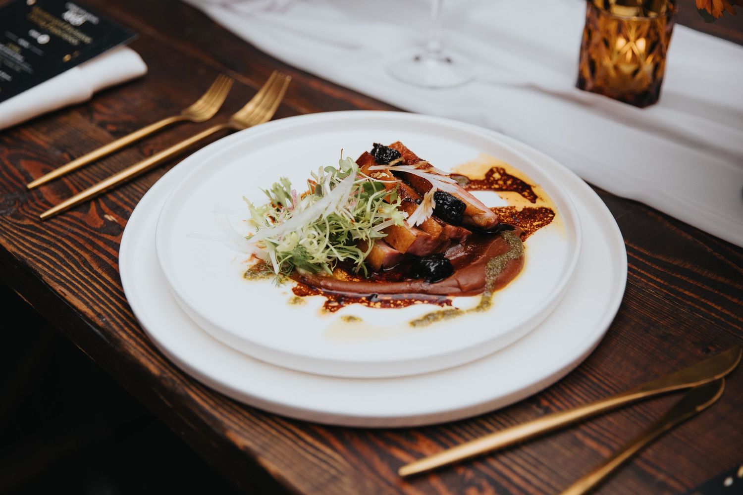 Beautifully plated gourmet dishes on white plates arranged on a dark wooden table.
