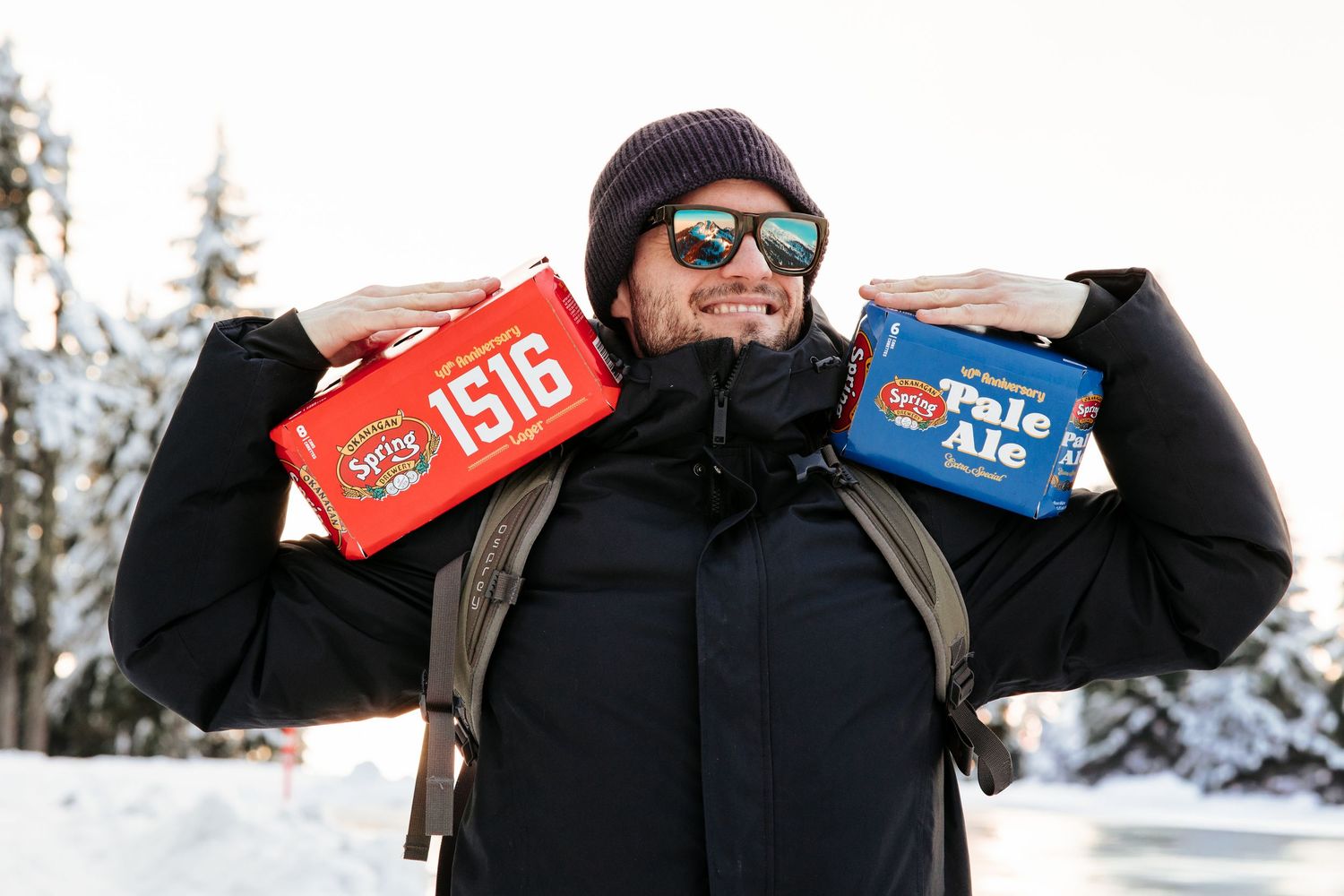 Person in winter clothing carrying beer cases through a snowy outdoor setting.