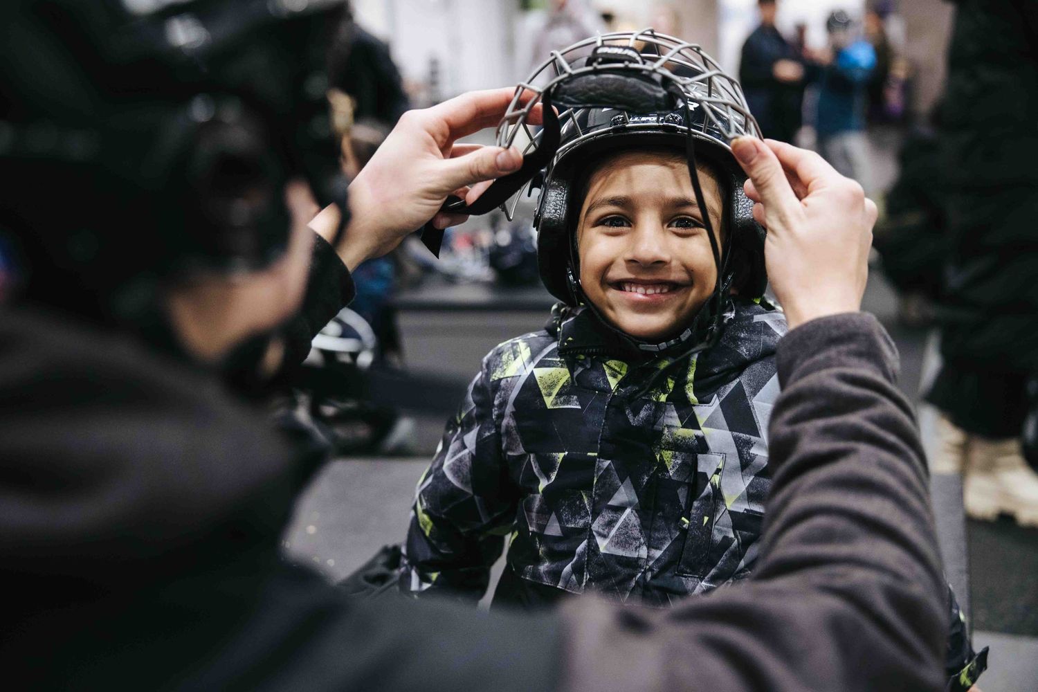 Someone adjusting a black helmet on another person wearing geometric patterned clothing.