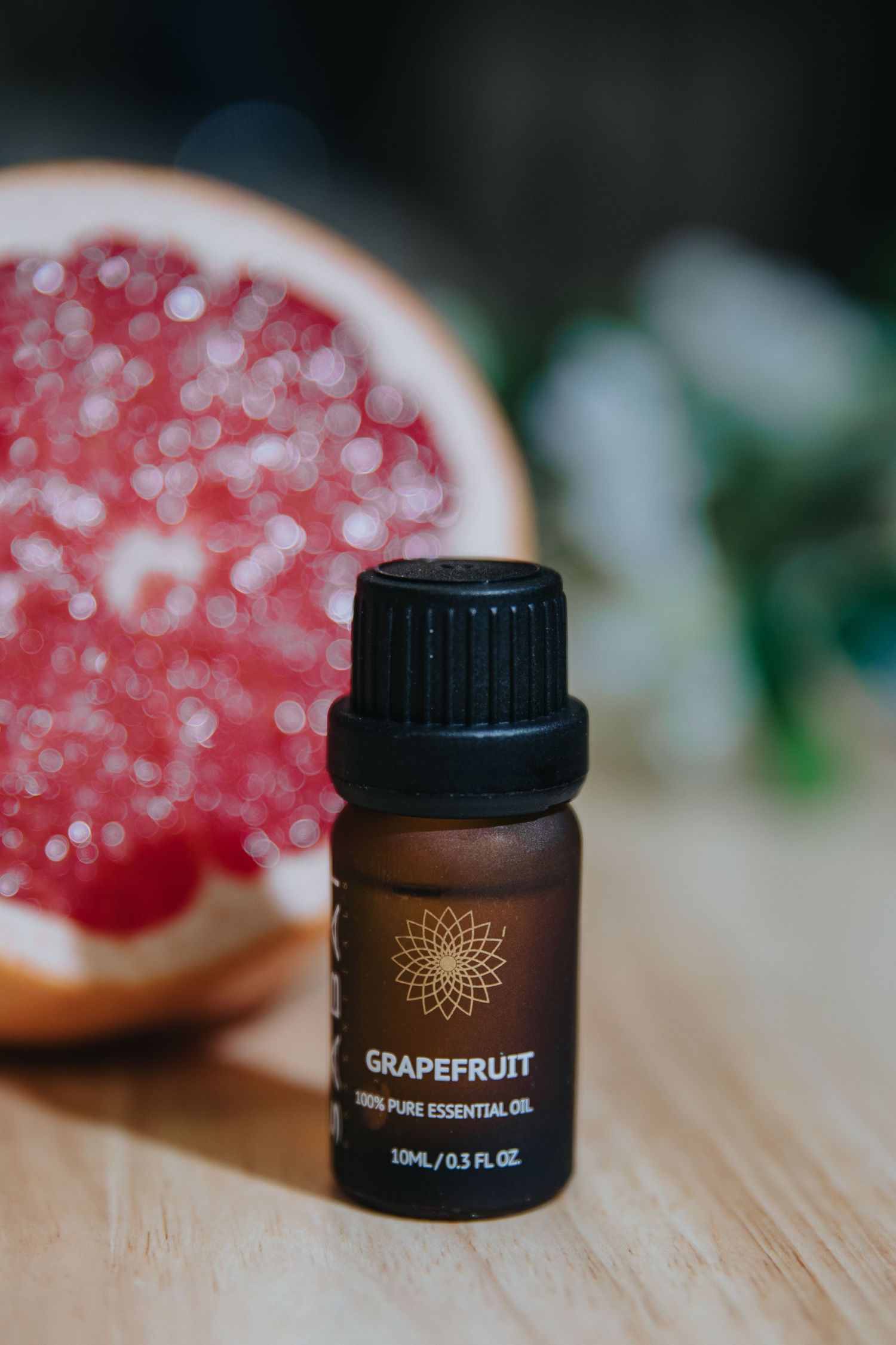 Close-up of grapefruit essential oil bottle with fresh citrus fruit in the background.