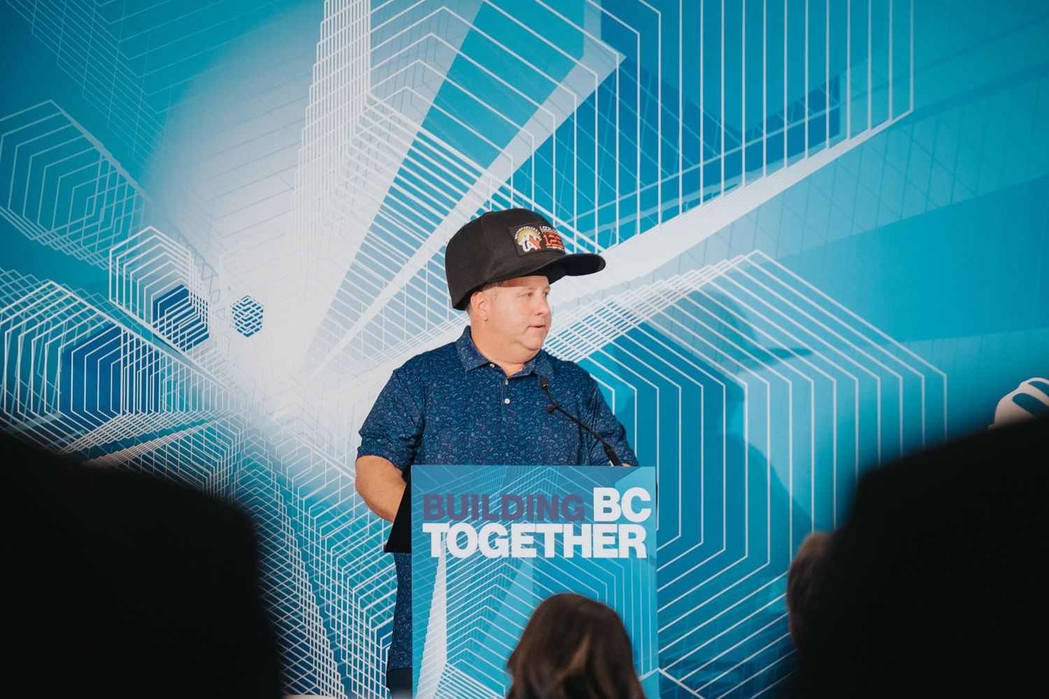 A speaker at a podium with a Building BC Together sign addresses an audience at an event.