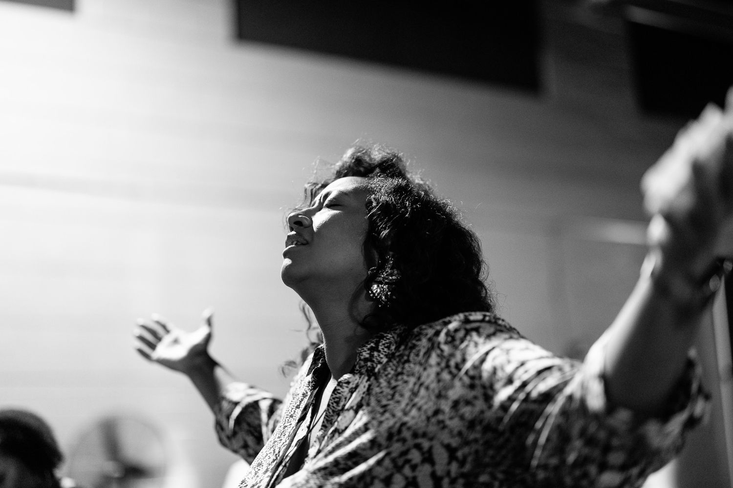 Black and white photo of woman with arms raised looking upward in expressive worship pose.