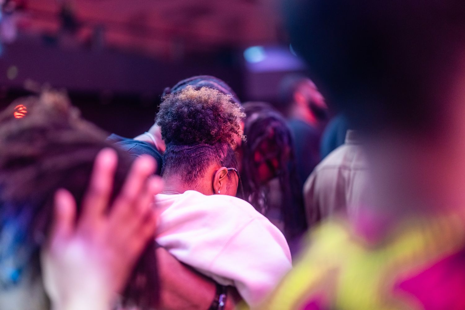 People embracing at a vibrant concert event with colorful purple and pink stage lighting in the background.