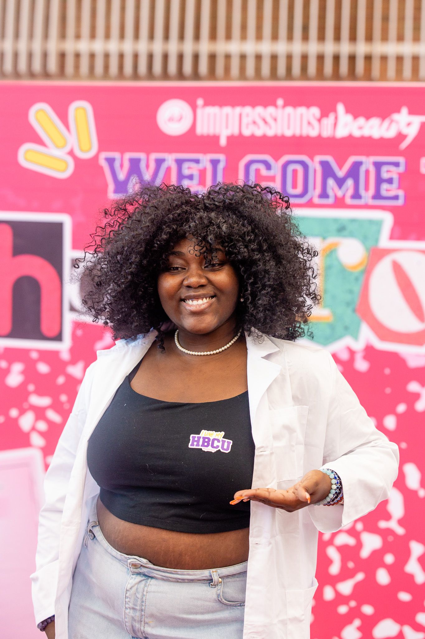 Smiling young woman with curly hair wearing HBCU crop top and white blazer posing at Impressions of Beauty event.