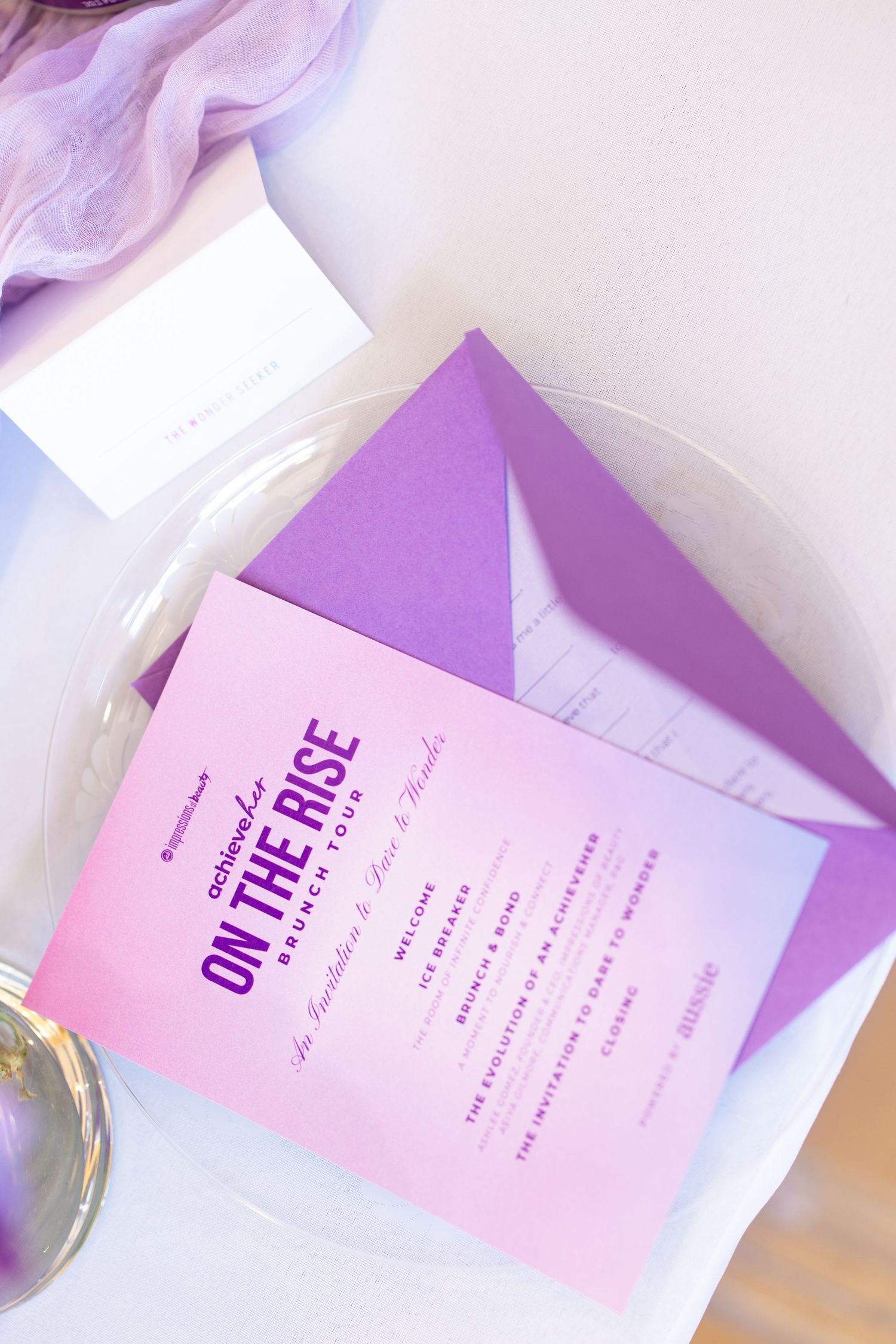 Purple gradient invitation card for On The Rise Brunch Tour event displayed on white plate with matching envelope.