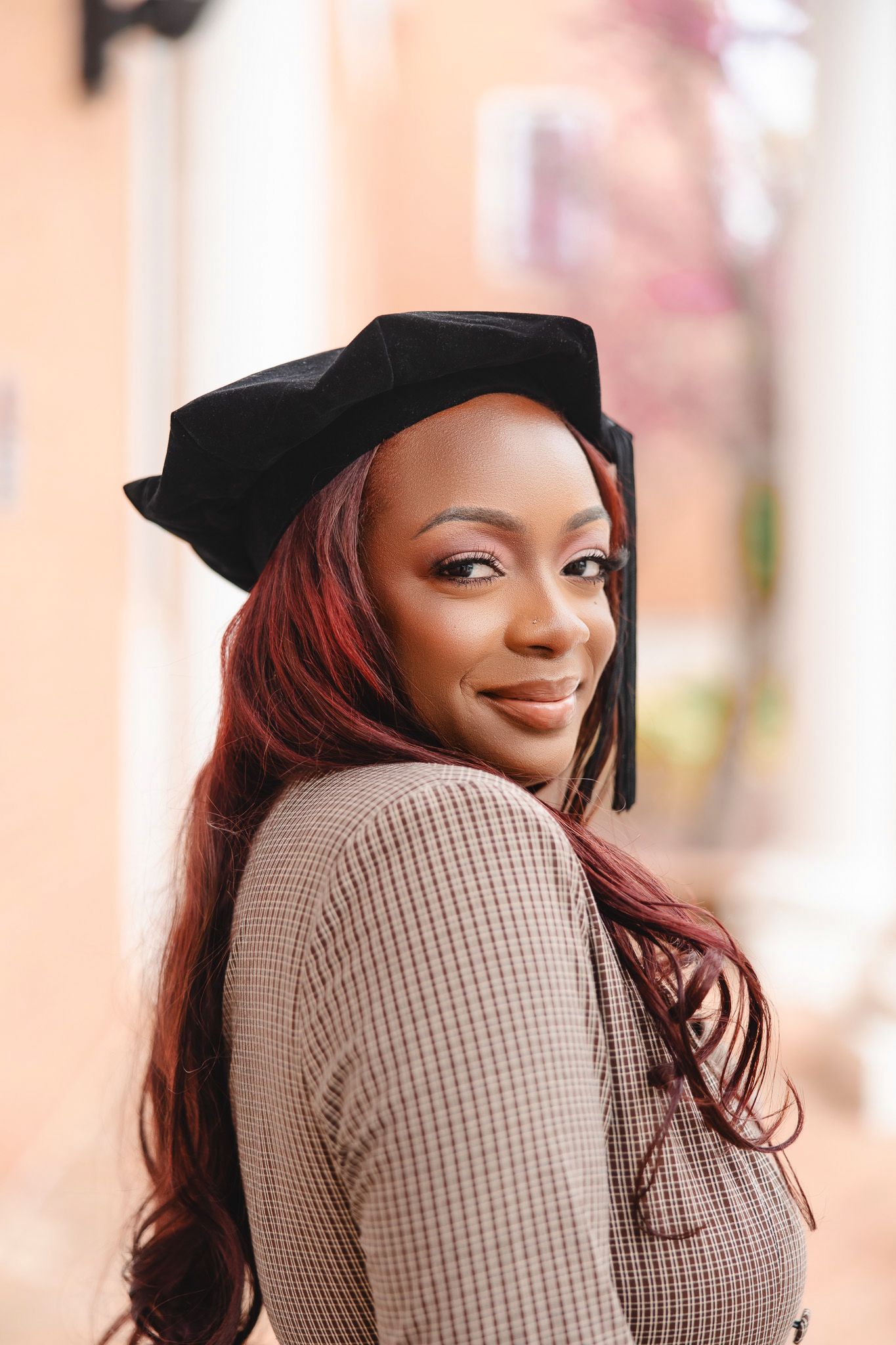 Graduate in black cap and beige sweater poses for celebratory photos.
