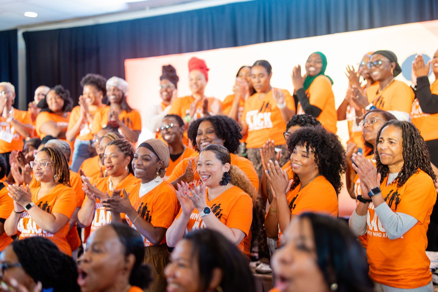 Crowd of people in orange shirts reacting enthusiastically at an event.
