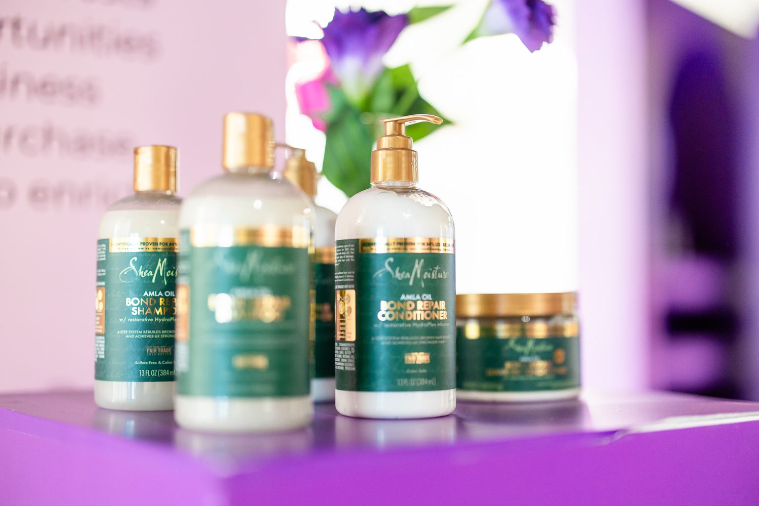 SheaMoisture hair care products with gold pumps displayed on a purple surface at a promotional event.