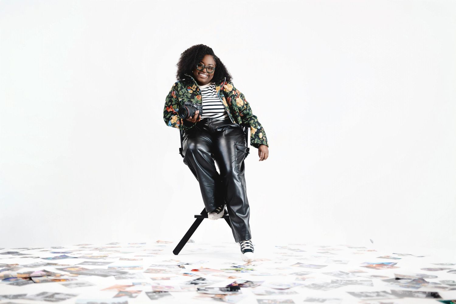 Person in a floral jacket and striped shirt poses playfully against white background.