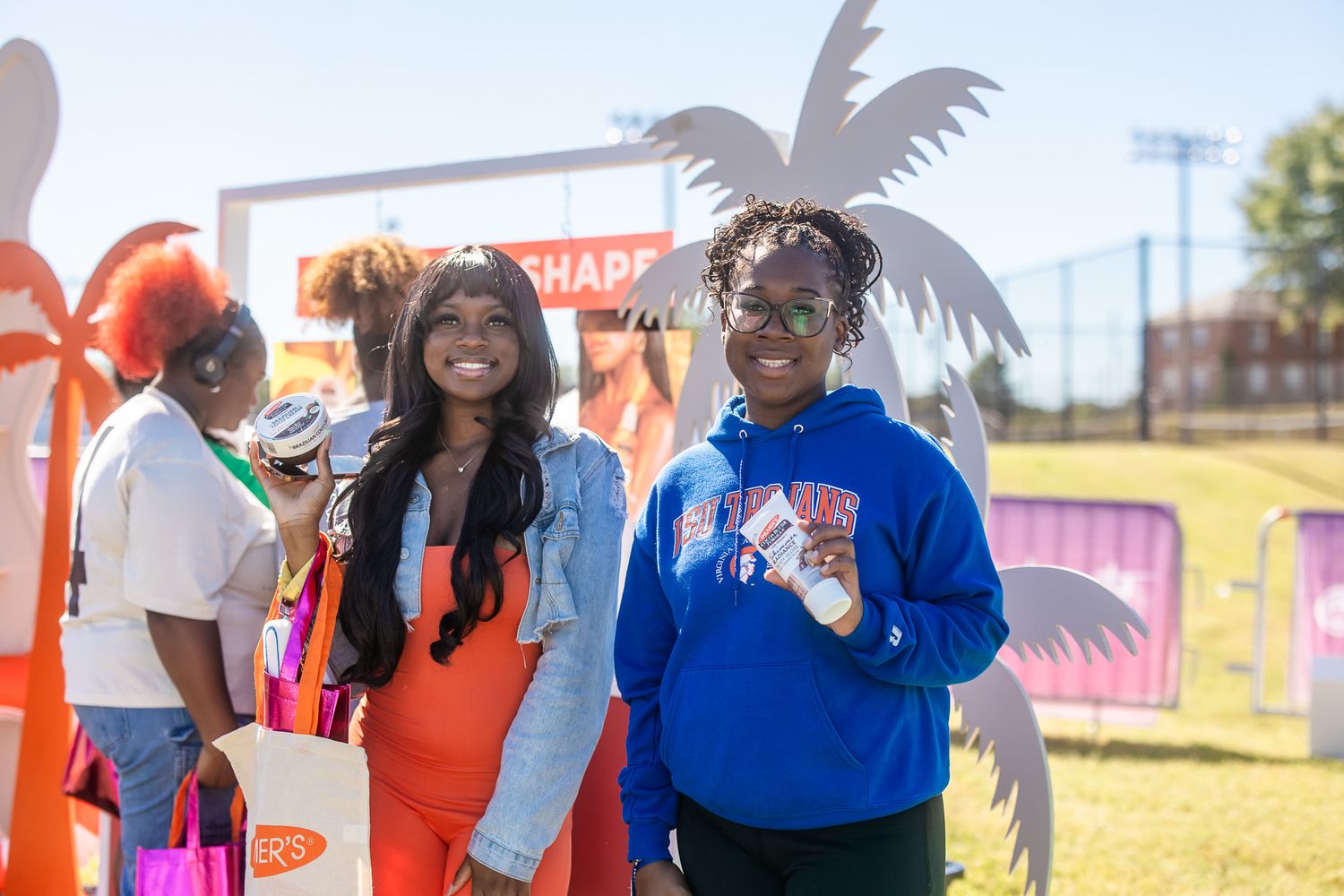 Two young women smiling outdoors at a festive event with colorful flamingo decorations on a sunny day.