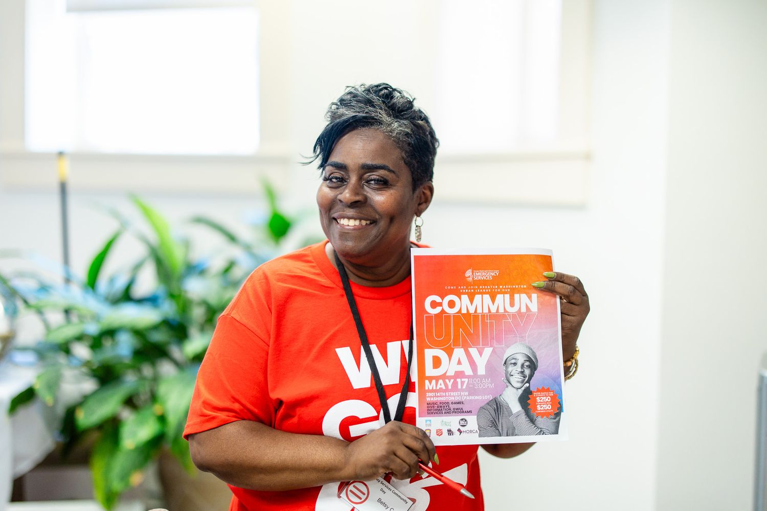 People in orange shirts displaying community engagement materials in a bright office setting.