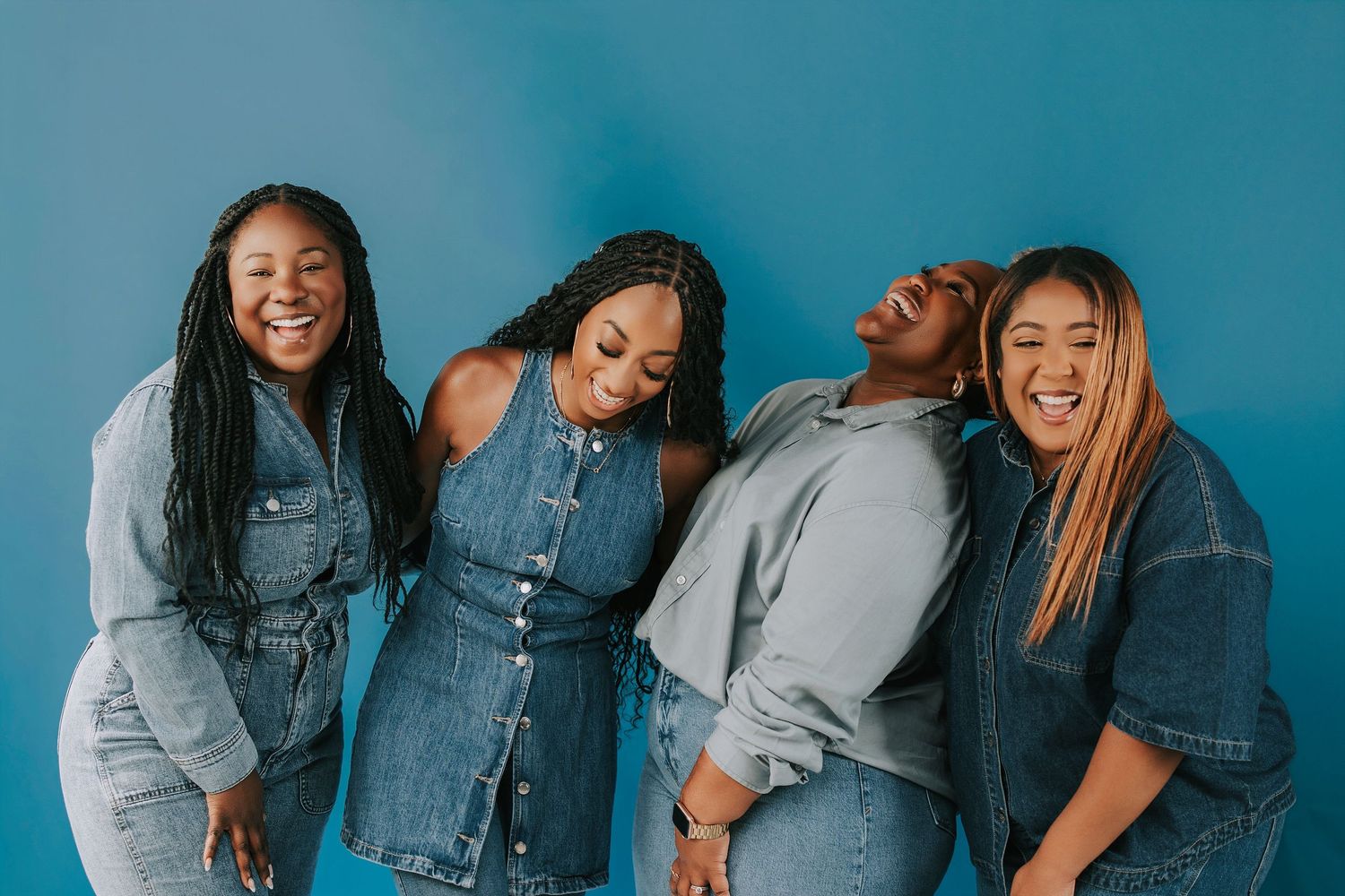 Group wearing denim outfits posing playfully against blue background.