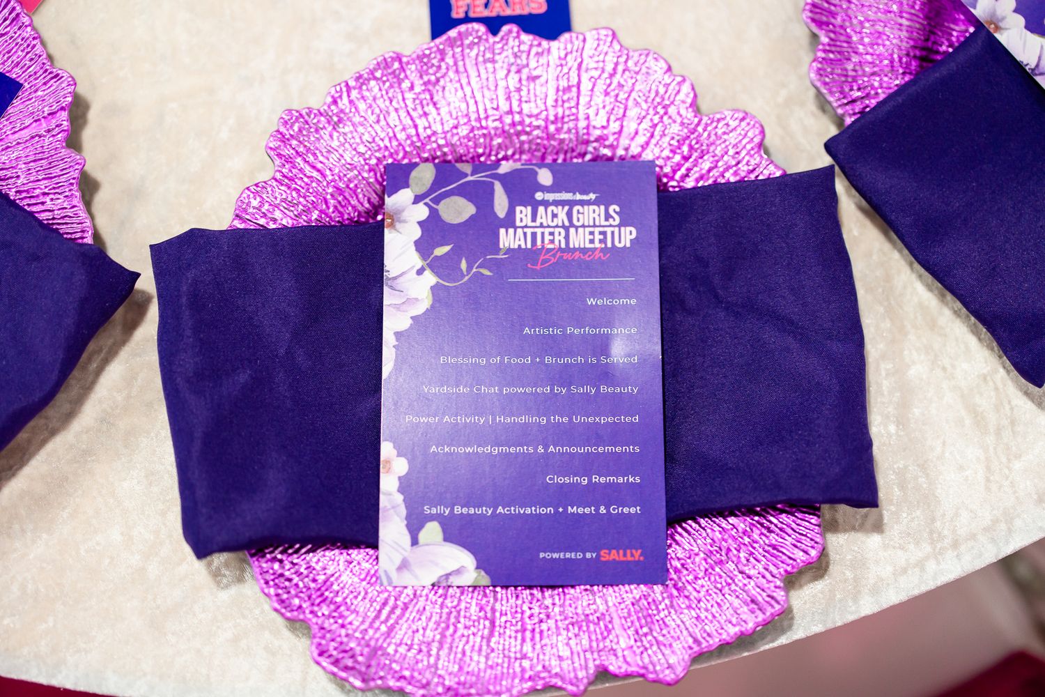 Purple program card for Black Girls Matter Meetup event displayed on decorative pink sequined charger plate.
