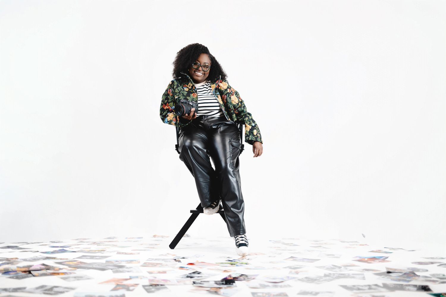 Young girl in floral jacket, leather pants, and sneakers posing confidently on confetti-covered floor.