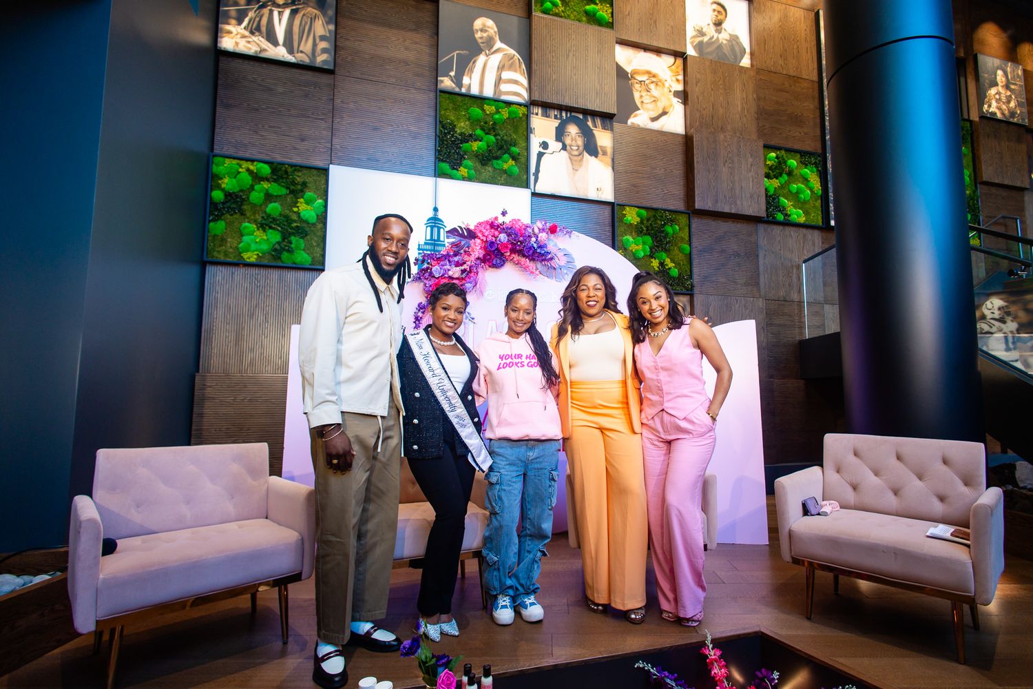 A family of five poses together in a modern lobby, with one woman wearing a pageant sash and crown.