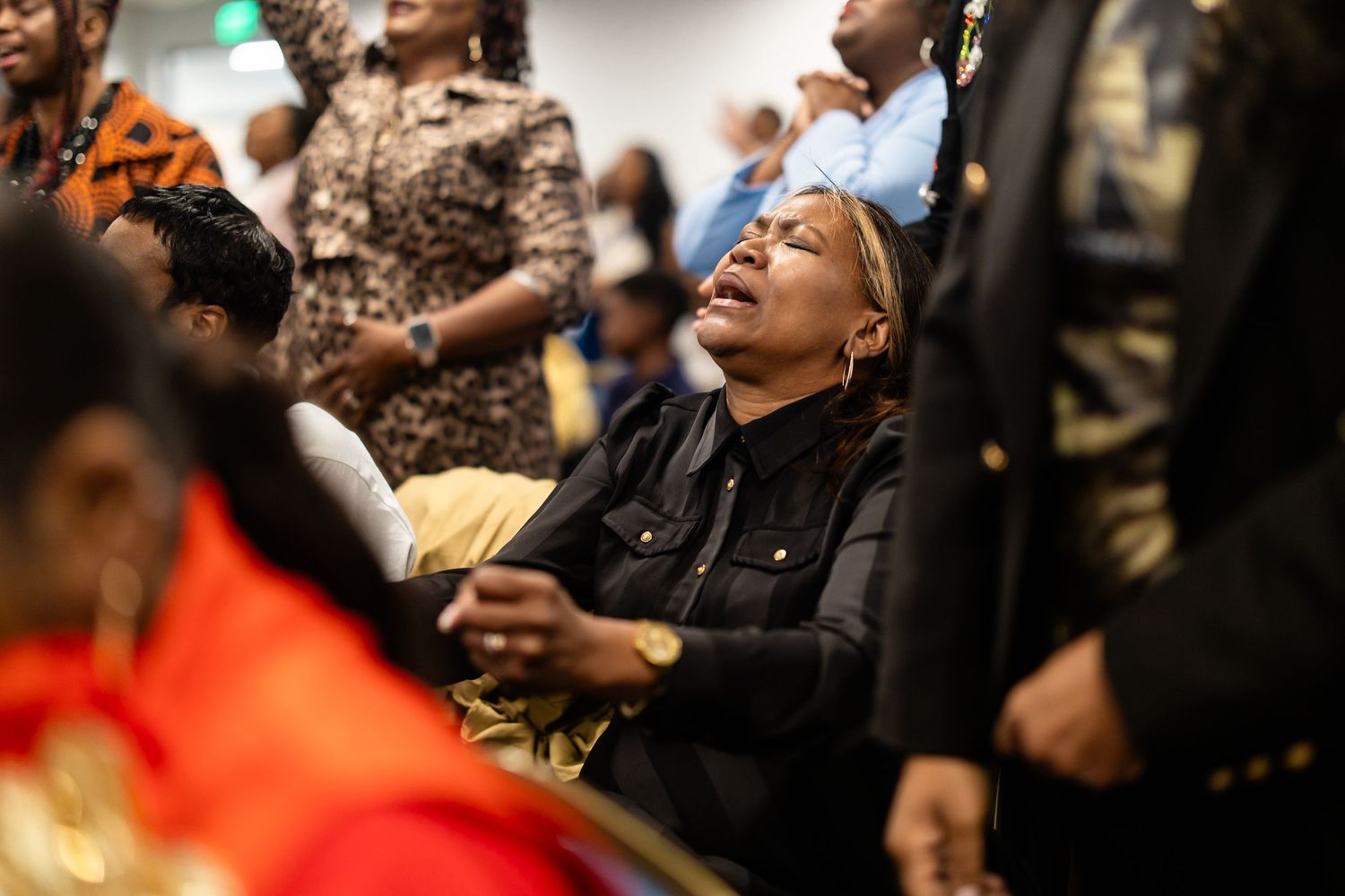 Emotional woman in black jacket at a crowded gathering, expressing deep feeling among diverse attendees.