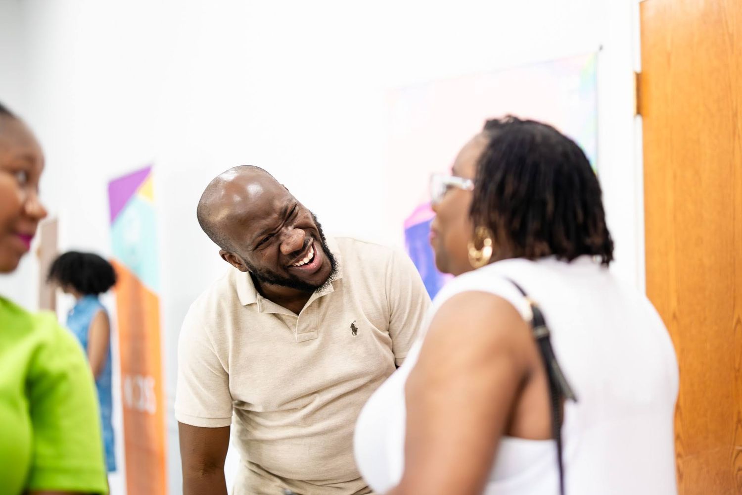 Three people laughing and conversing in a bright room, with a man in a beige polo shirt sharing a joyful moment.