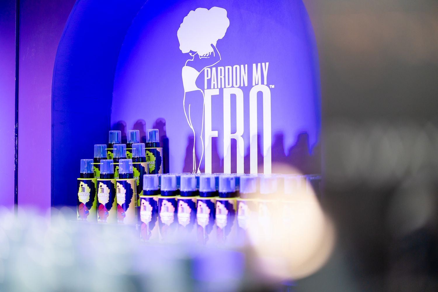 Pardon My Fro branded display with stacked products illuminated by purple lighting at an event.