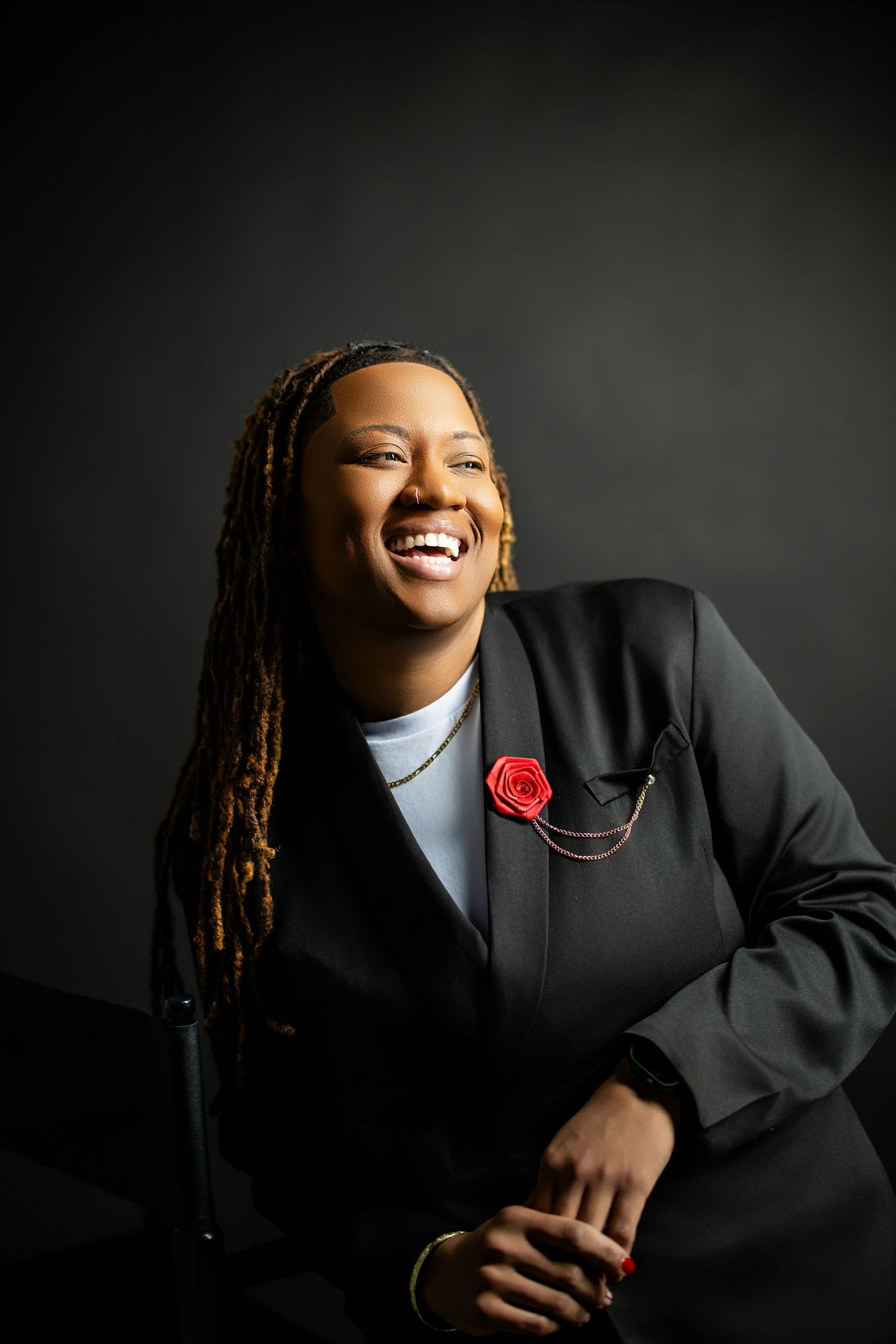 Dramatic studio portraits against dark background featuring someone in formal attire with a red flower accent.