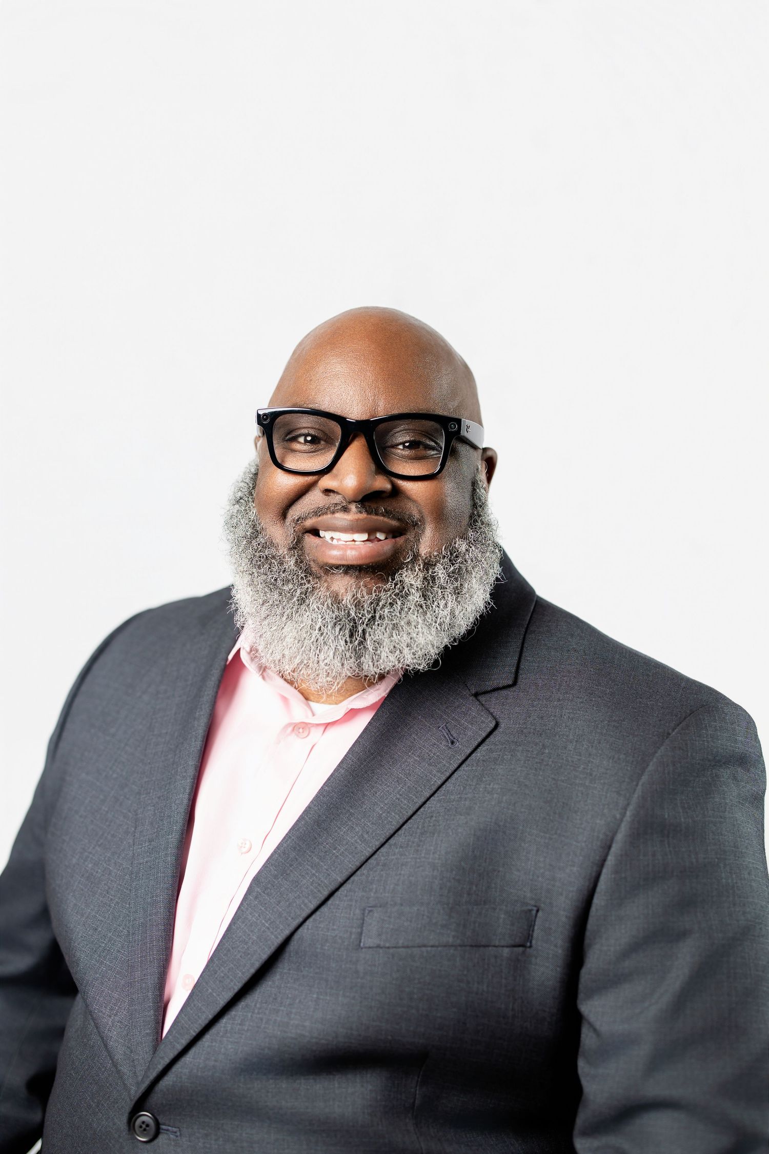 Professional headshot series of a person with glasses and a gray beard wearing a dark suit and pink shirt.