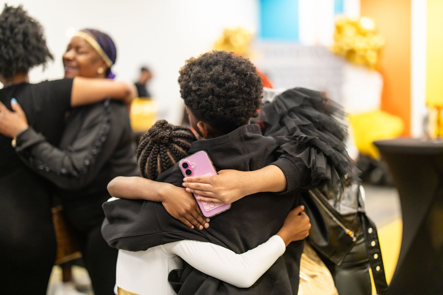 People in black attire sharing warm embraces at an indoor gathering or celebration event.