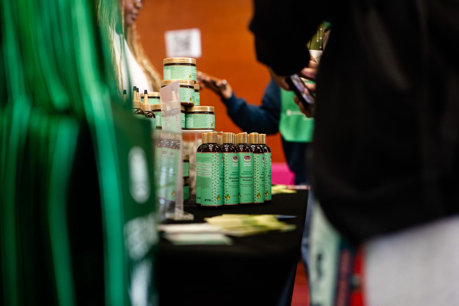 Green labeled bottles and jars displayed on a vendor table at an indoor market or trade show event.
