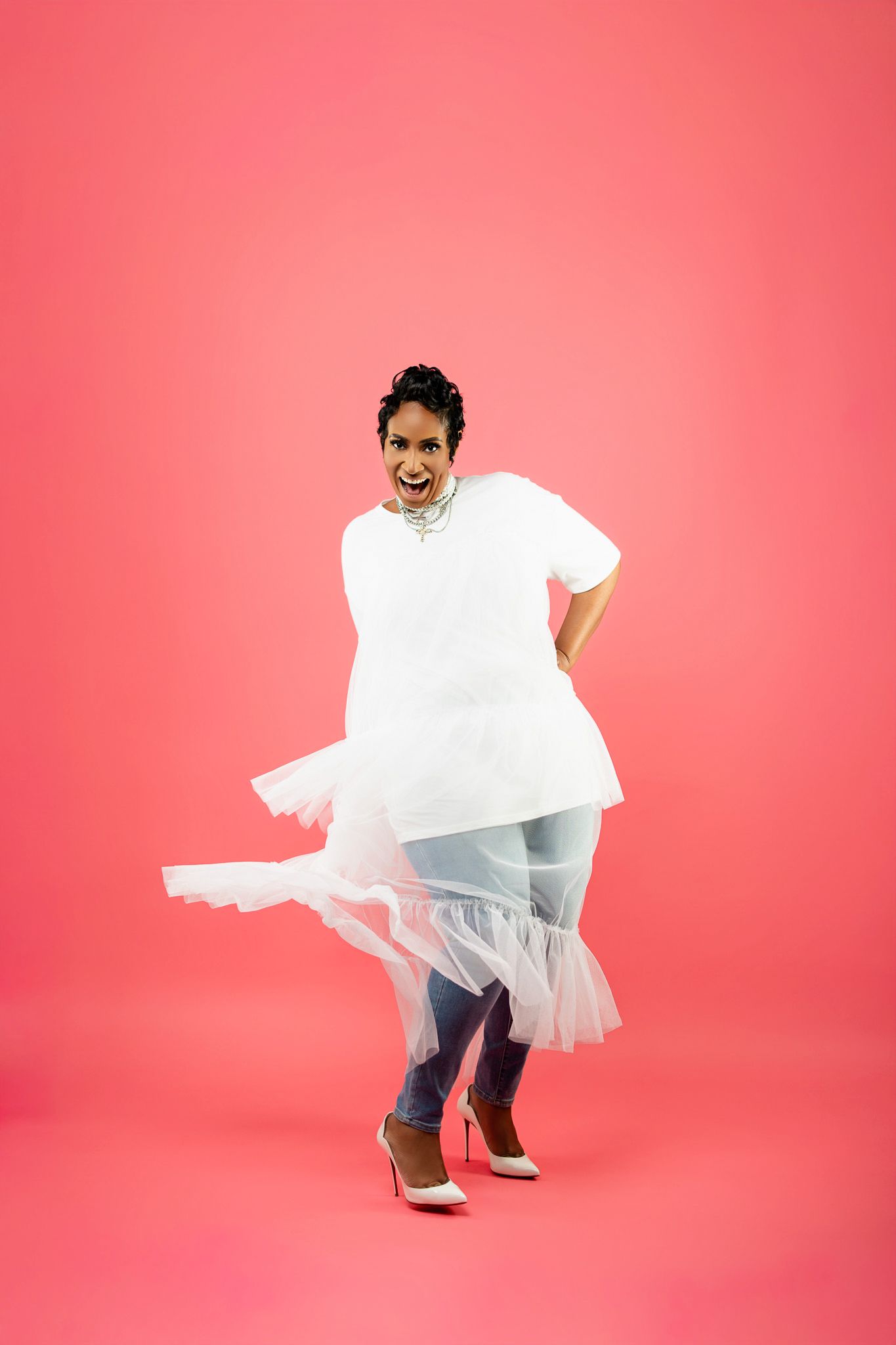 Person in white flowing dress twirling against pink background in studio setting.
