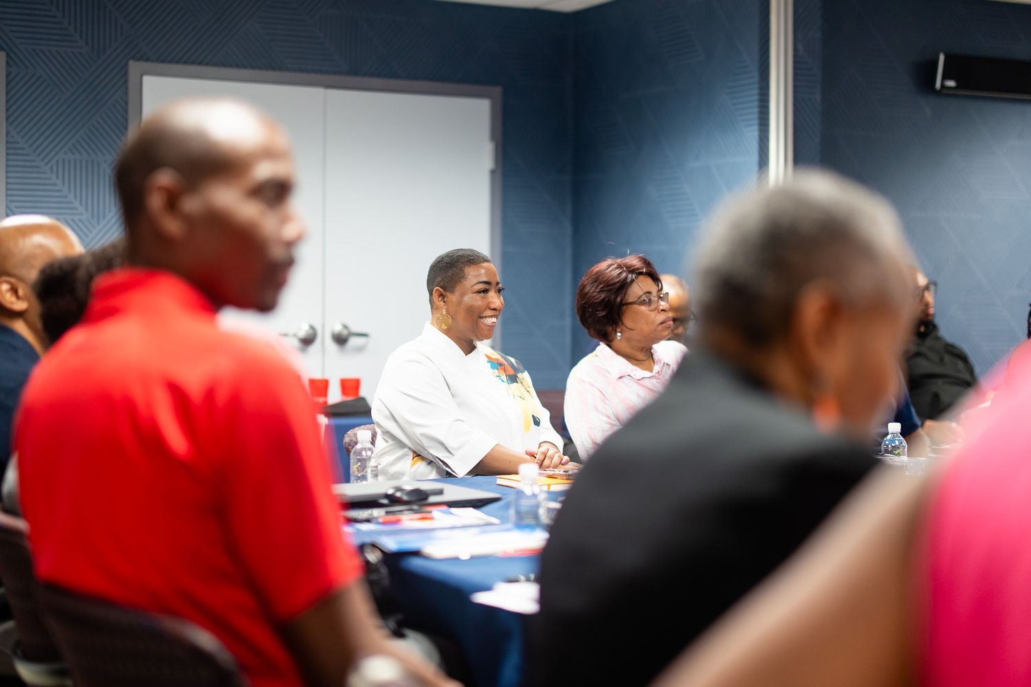 Meeting room scene with people seated at tables in business casual attire.