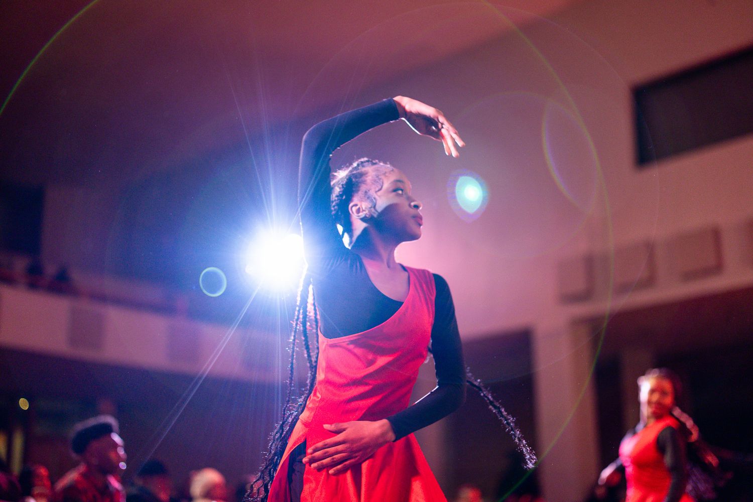 A dancer in a red costume performs gracefully under stage lights at a dance competition or showcase.