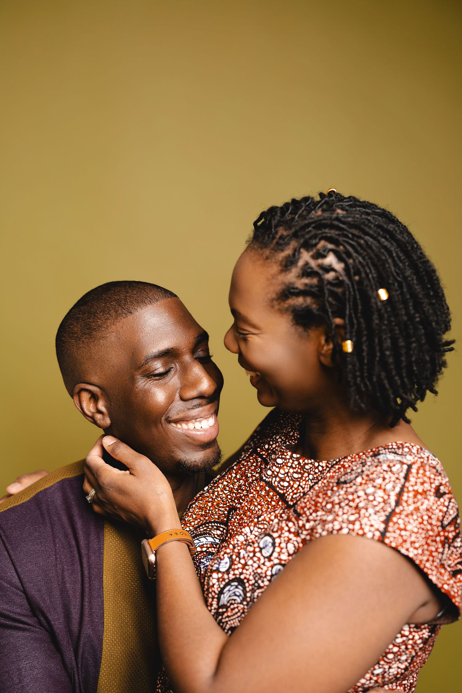 A joyful African couple sharing a tender moment, smiling at each other against an olive green background.