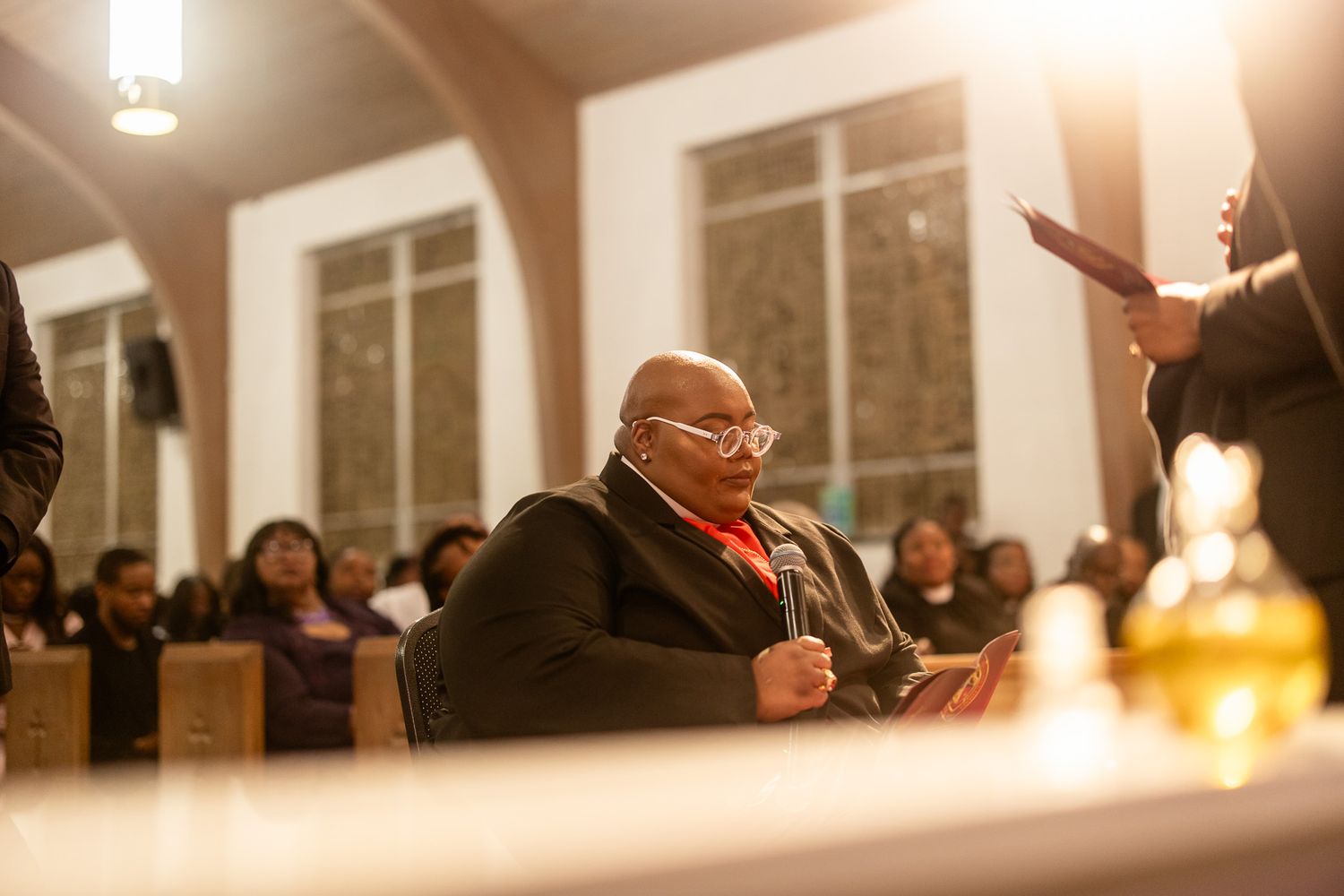 Elderly man with glasses and red bow tie seated in a warmly lit church during a formal evening gathering.