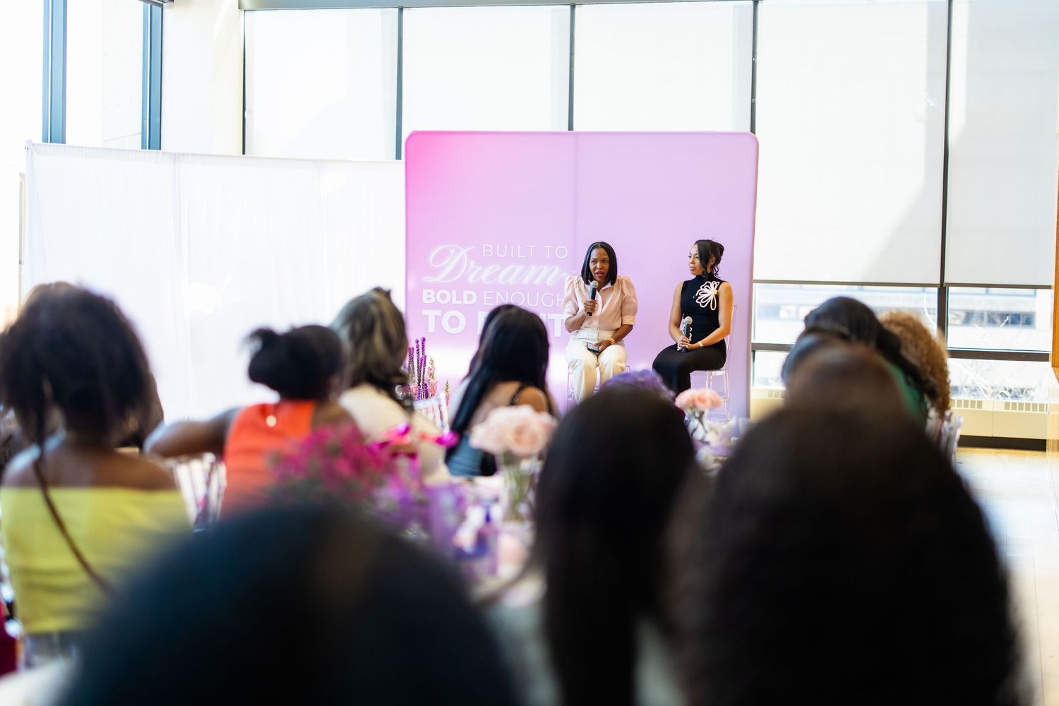 Two women speak on stage at a Dream conference event, seated before an audience of diverse attendees.