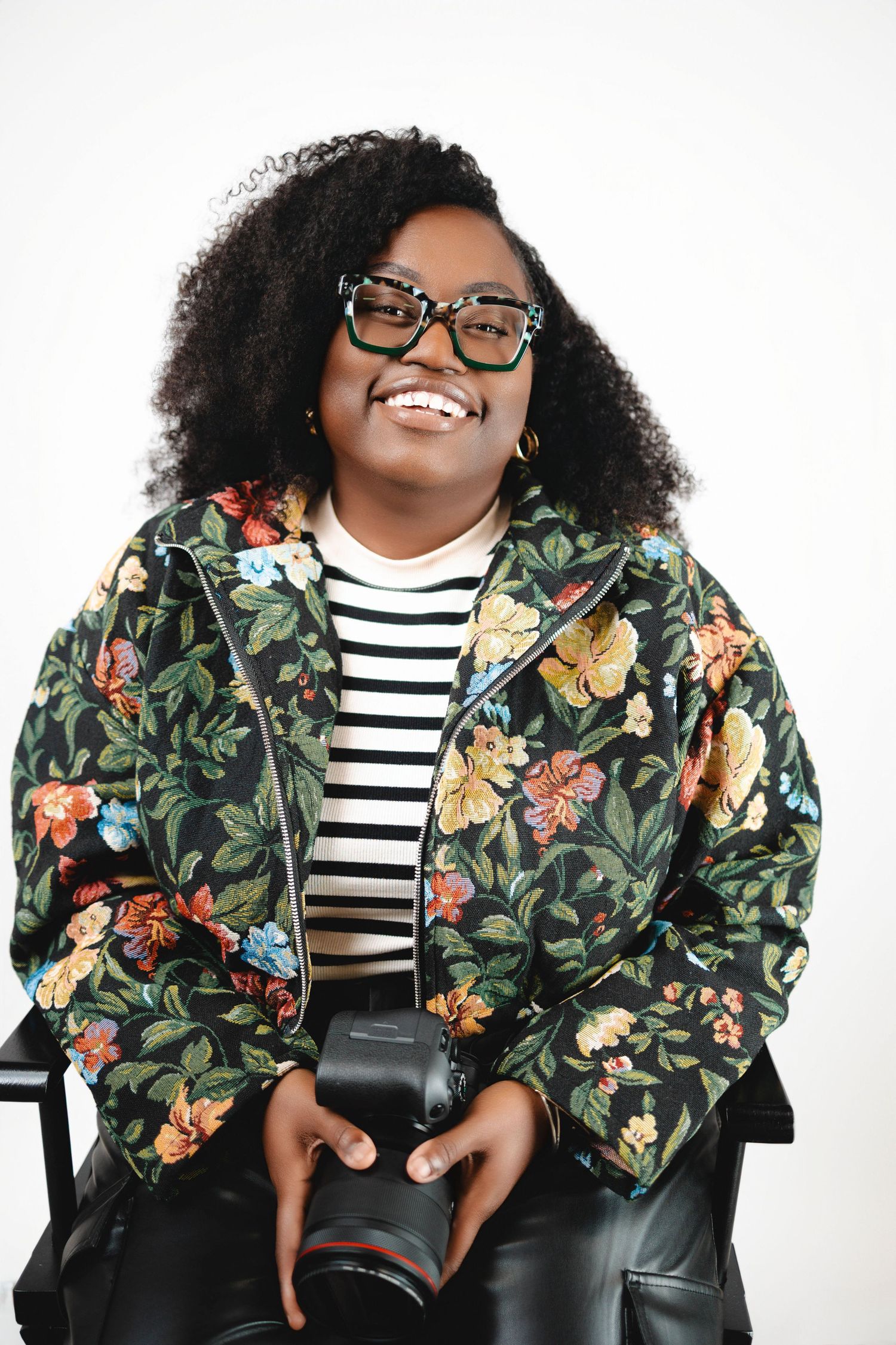 Stylish individual wearing floral bomber jacket and striped top in studio photoshoot.