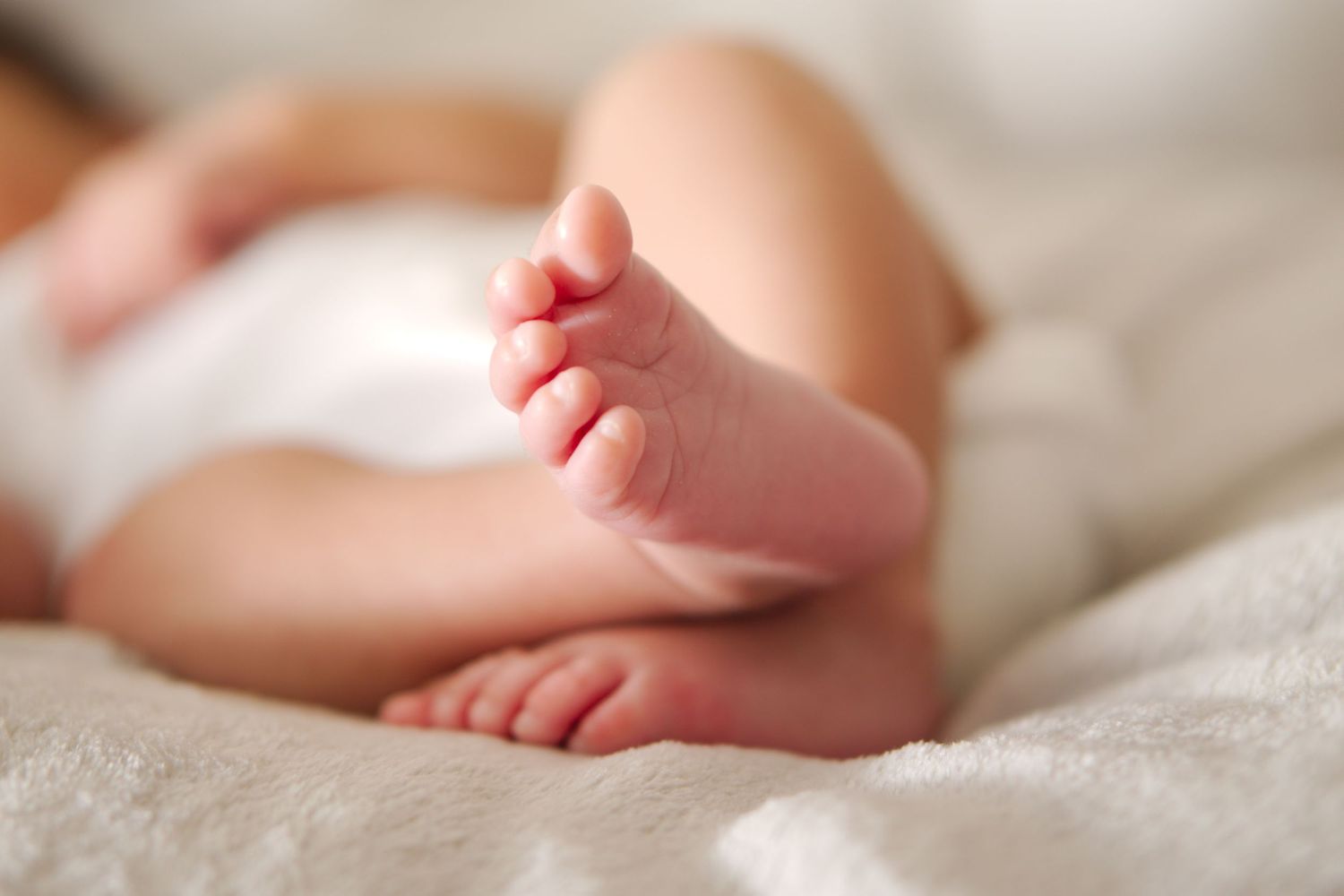 Close-up of newborn baby feet resting on a soft white blanket.