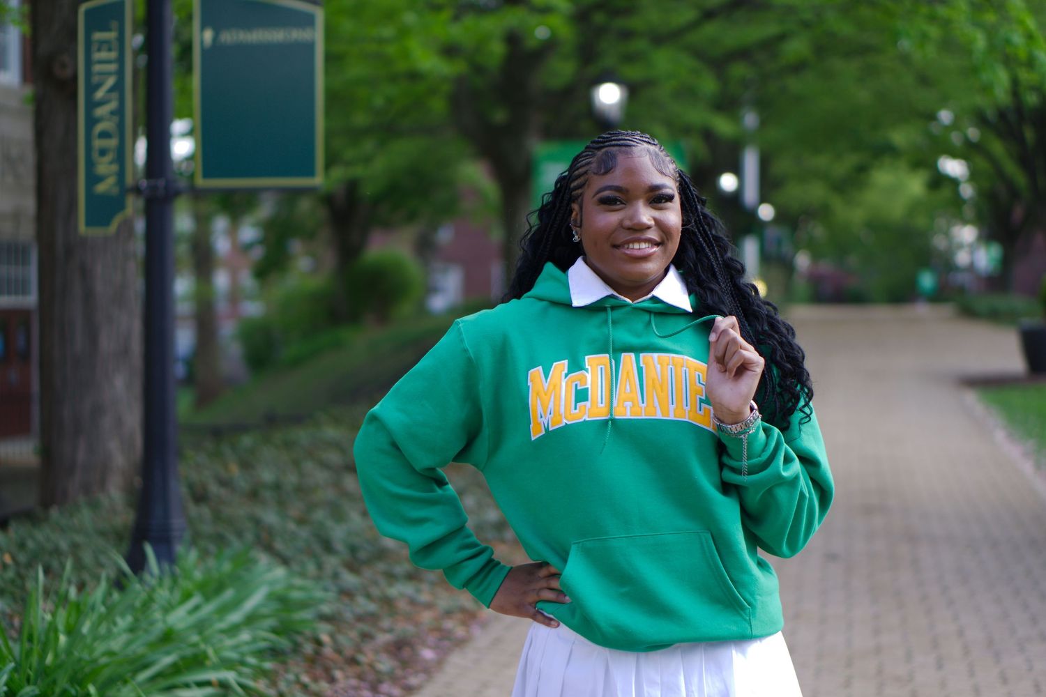 Smiling student in green McDaniel College sweatshirt posing on campus walkway.