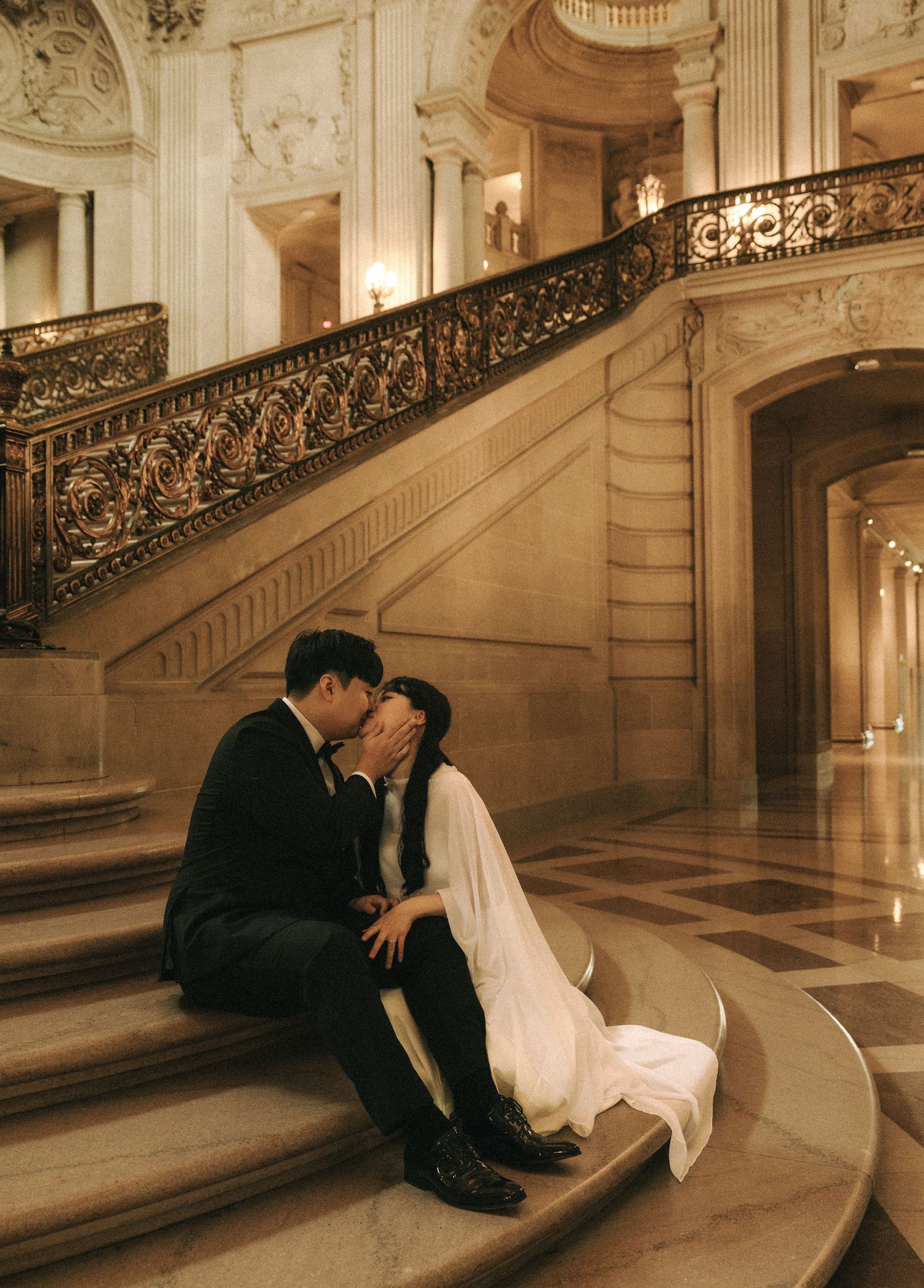 Couple sharing a romantic kiss on marble steps inside an elegant grand staircase hall.