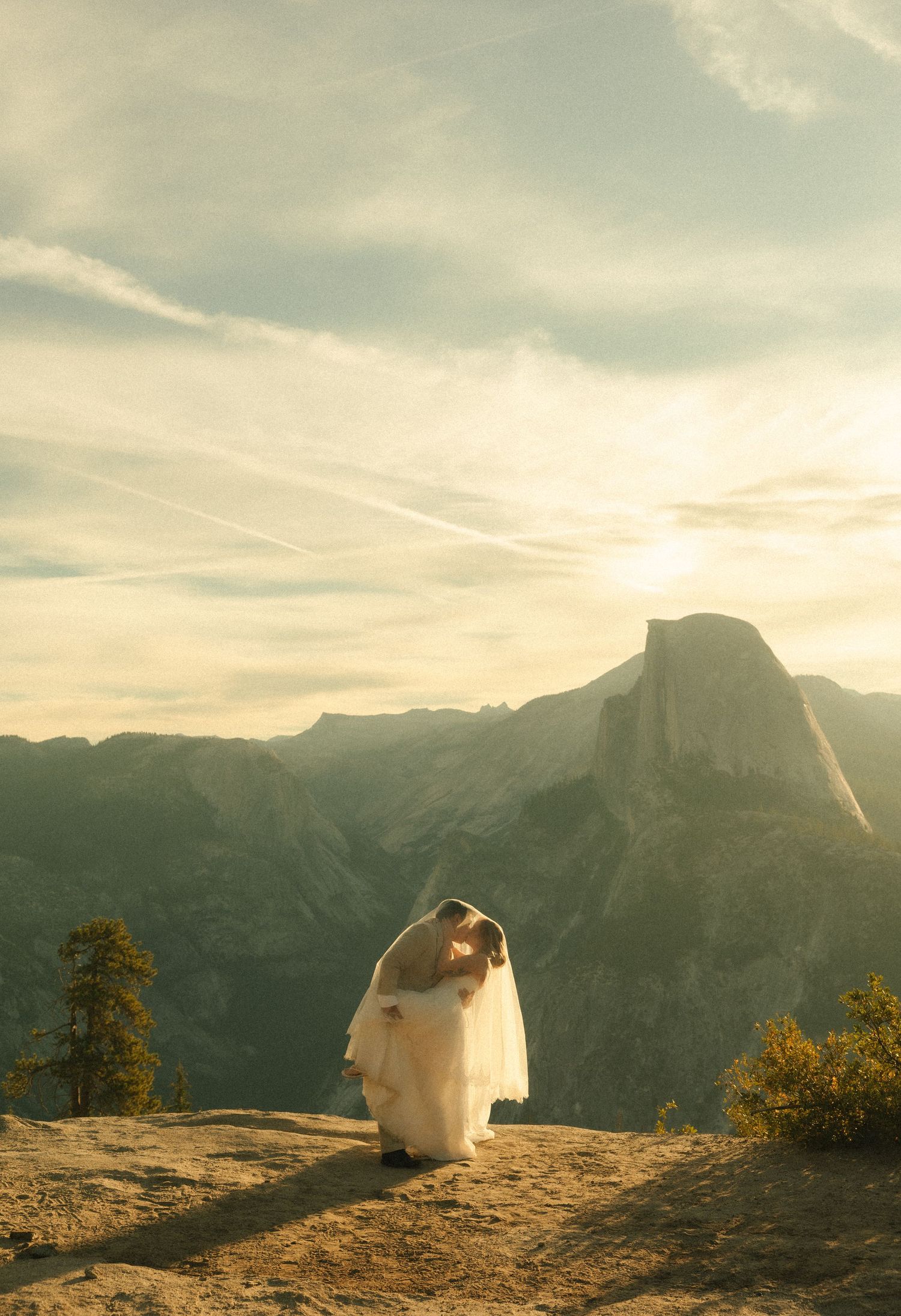 Couple embracing at Glacier Point, Yosemite, with Half Dome and golden sunset sky backdrop.