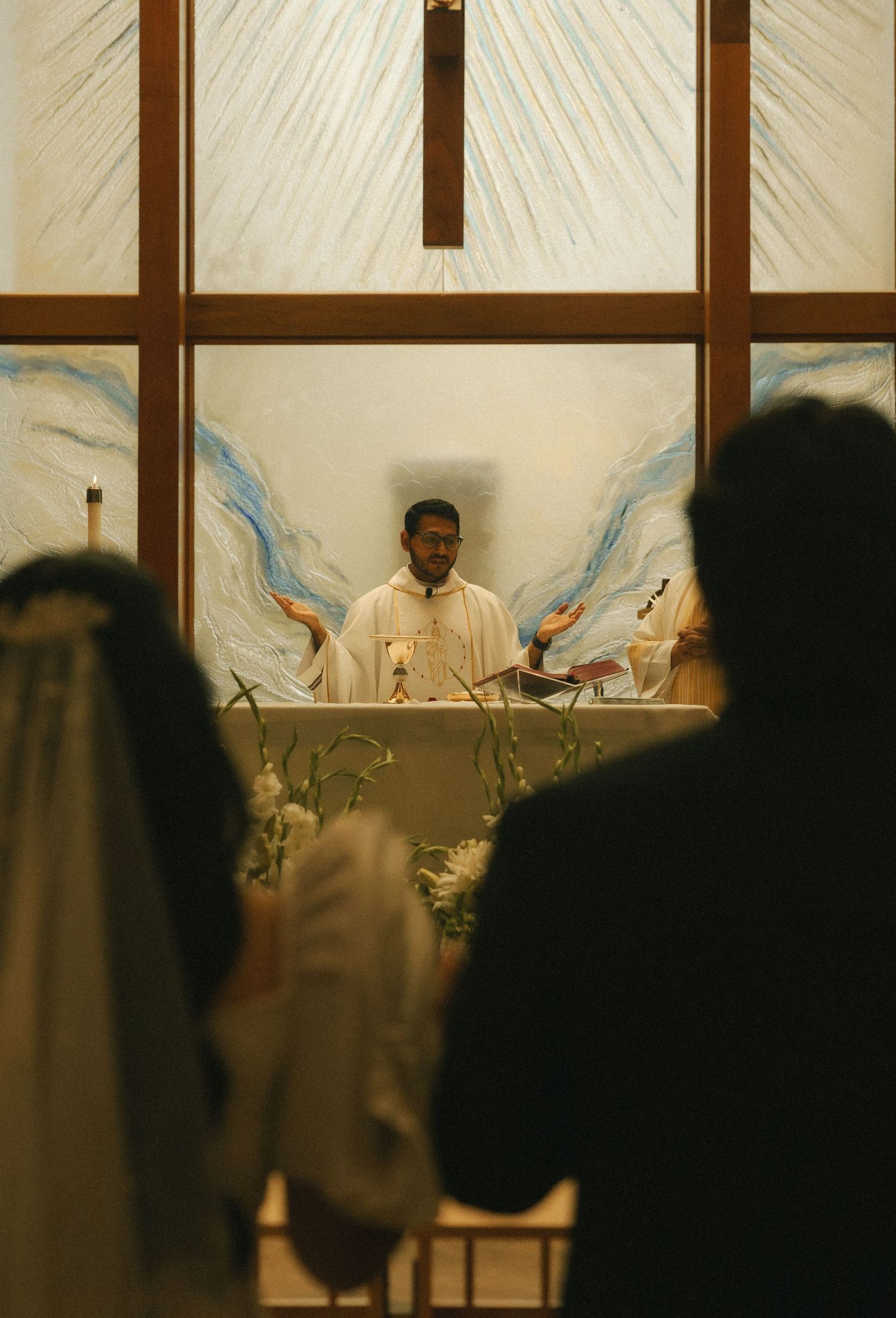 Priest officiating a wedding ceremony at a church altar with angel wing murals and a cross backdrop.